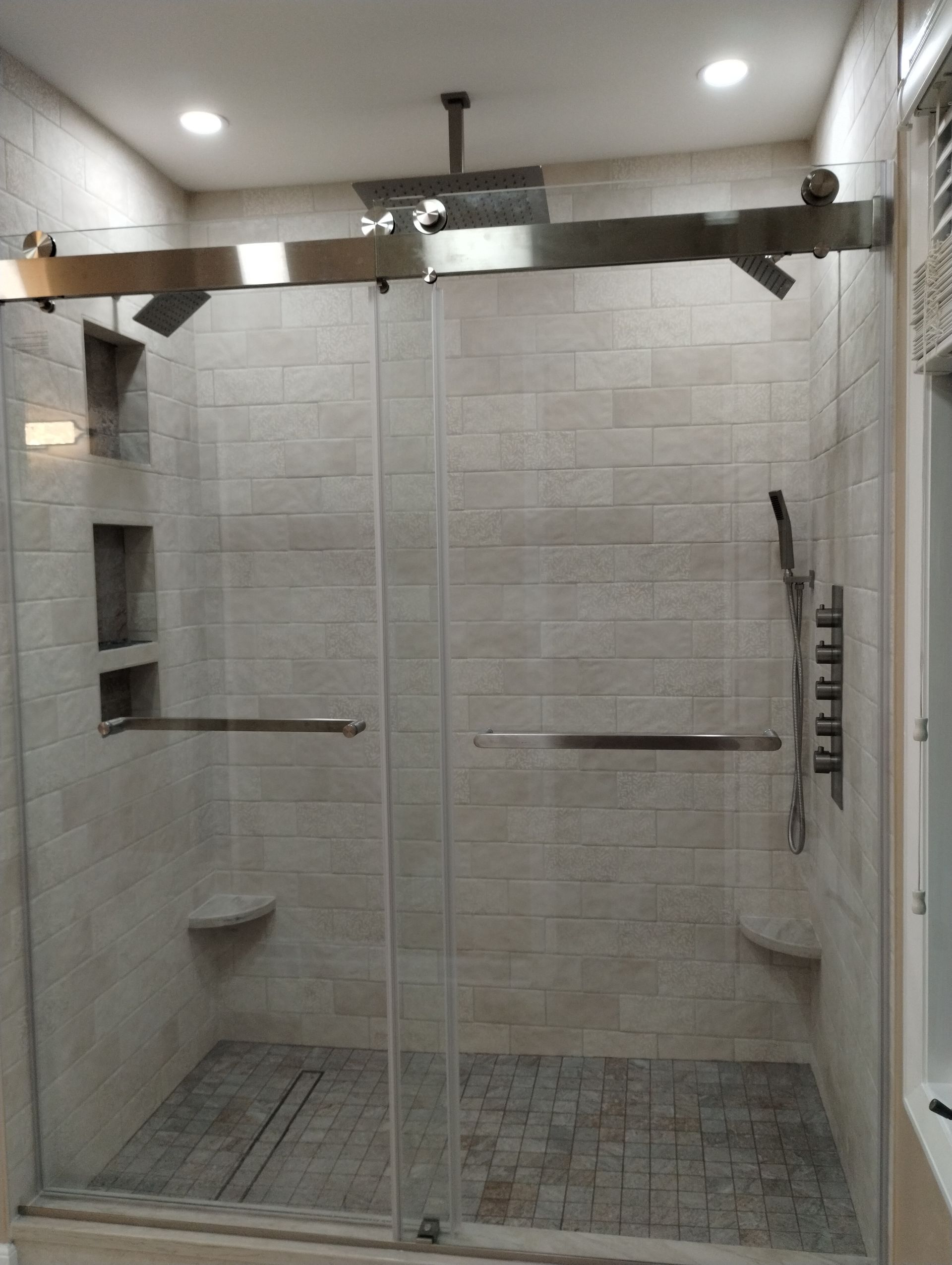 Modern walk-in shower with glass doors, tiled walls, built-in shelves, and overhead lights