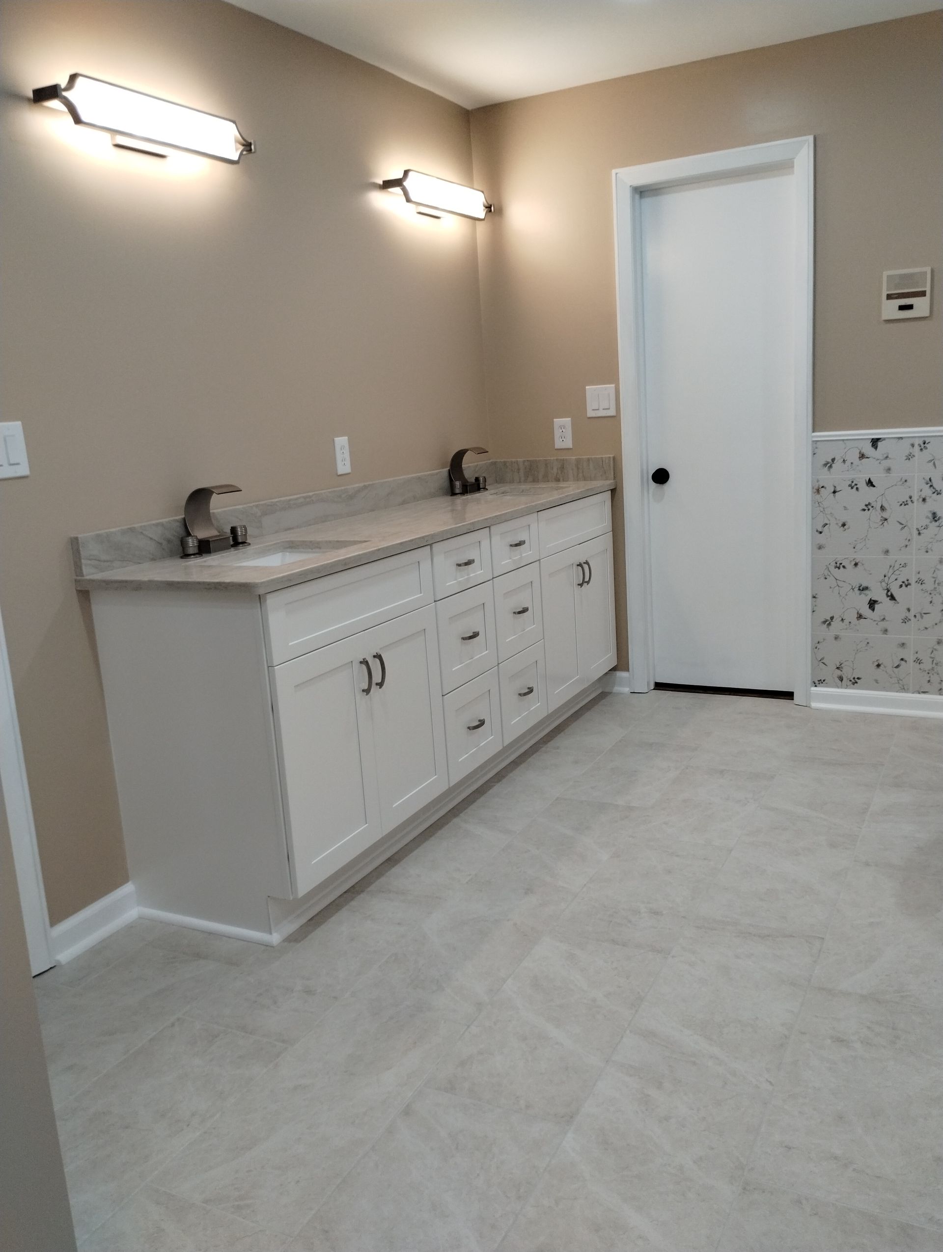 Modern bathroom with double vanity, wall sconces, white door, and light tile floor