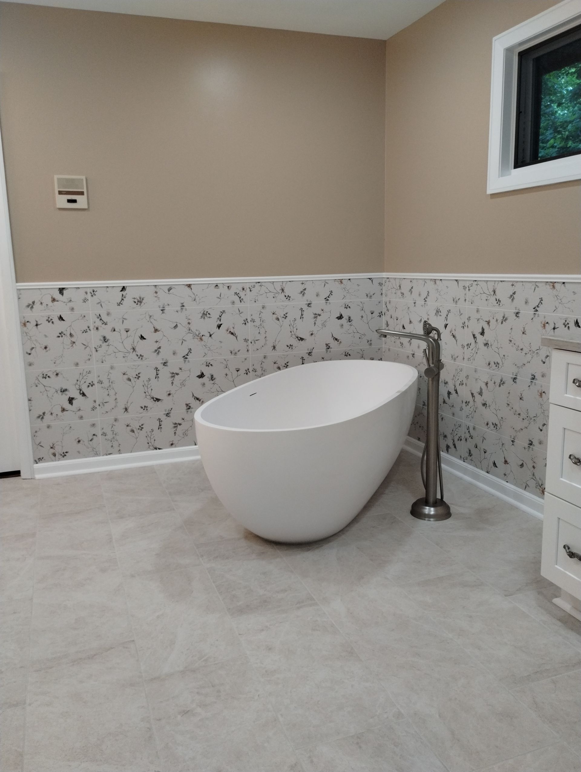 Modern bathroom with a freestanding white tub, speckled half-wall, and beige walls