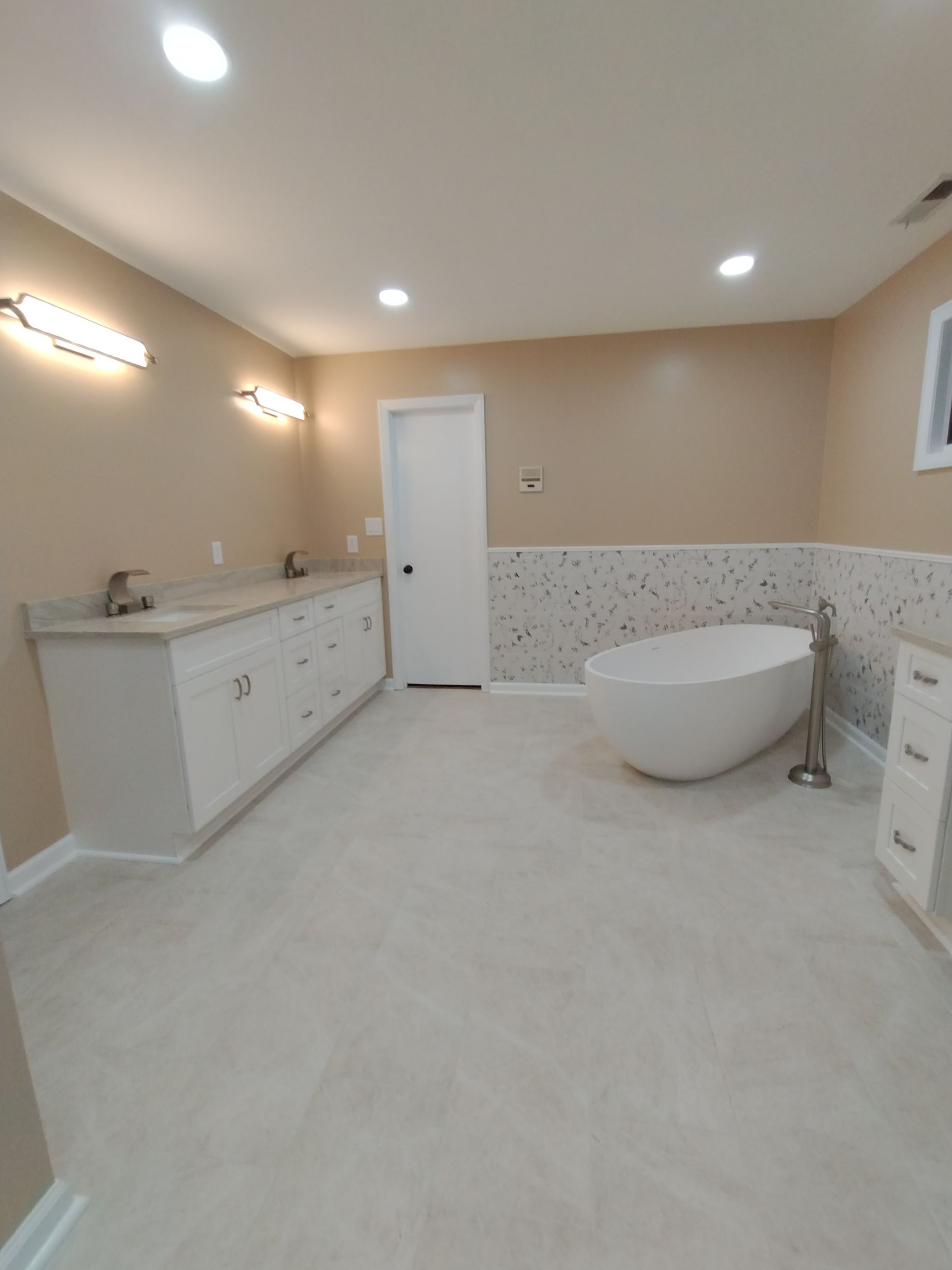 Spacious modern bathroom with double vanity, freestanding tub, light tile floor, and beige walls