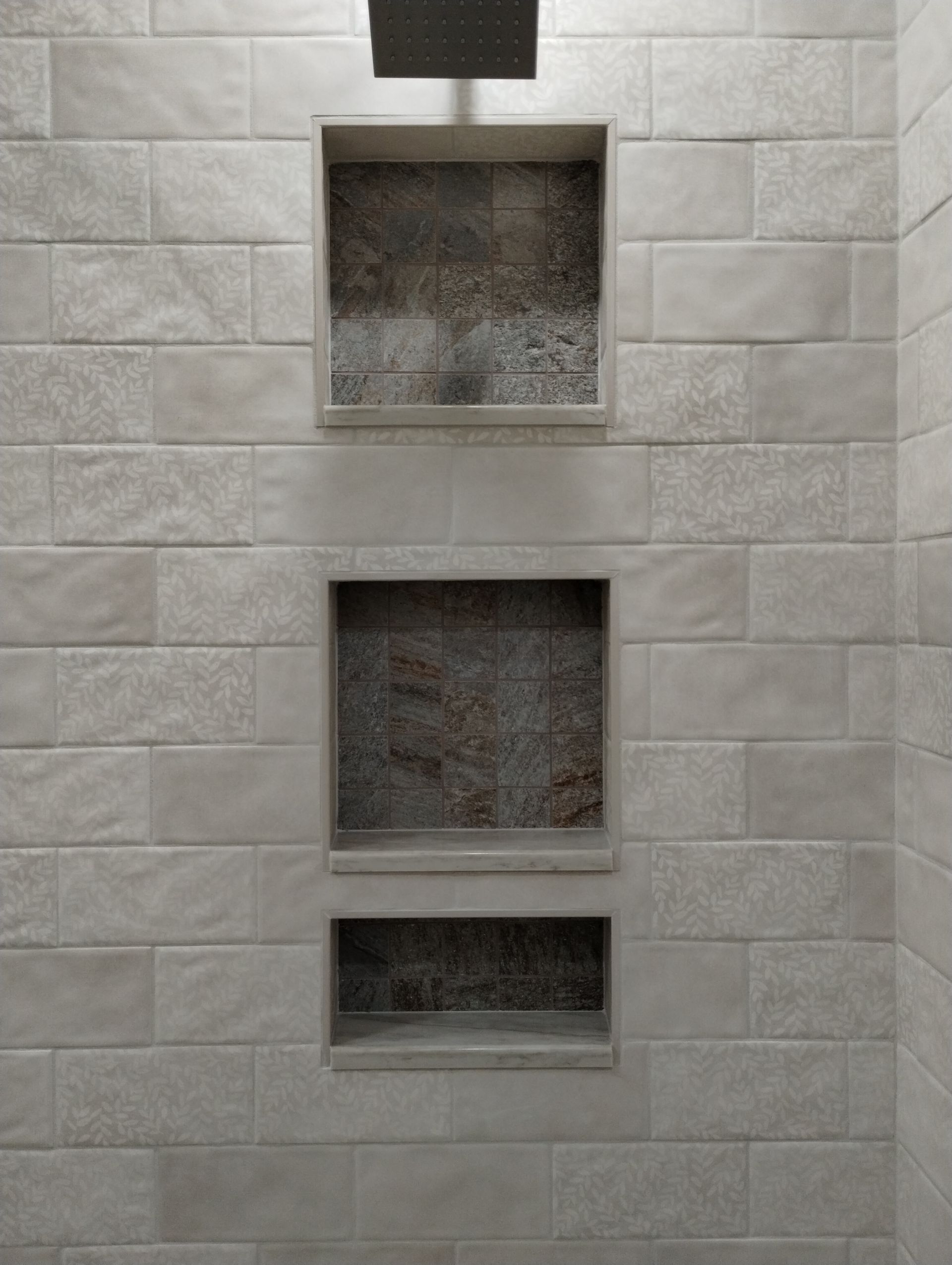 Stacked recessed wall niches in a light gray tiled wall, with a dark vent above.