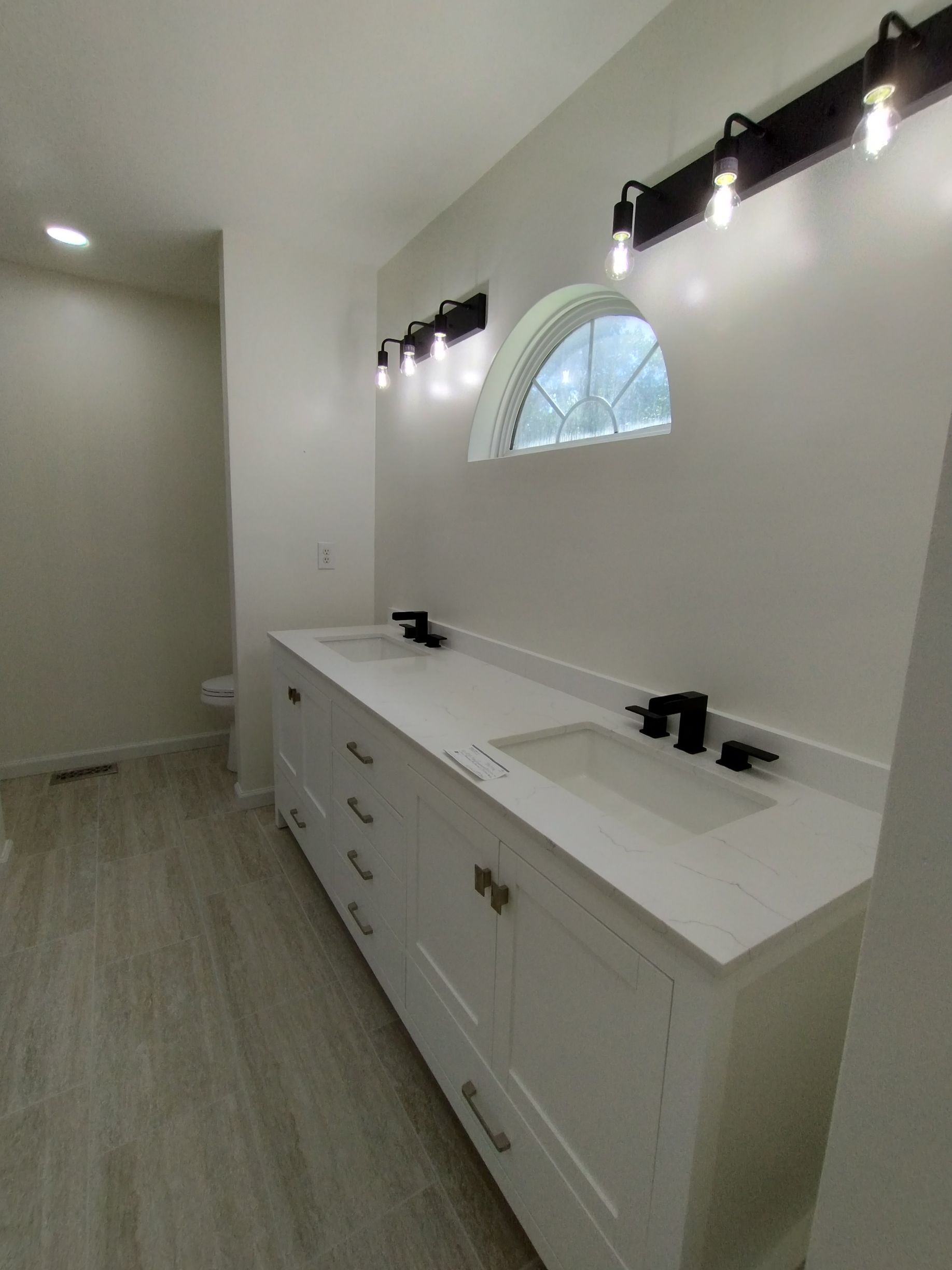 Modern bathroom with double sink vanity, white cabinets, wall lights, and an arched window