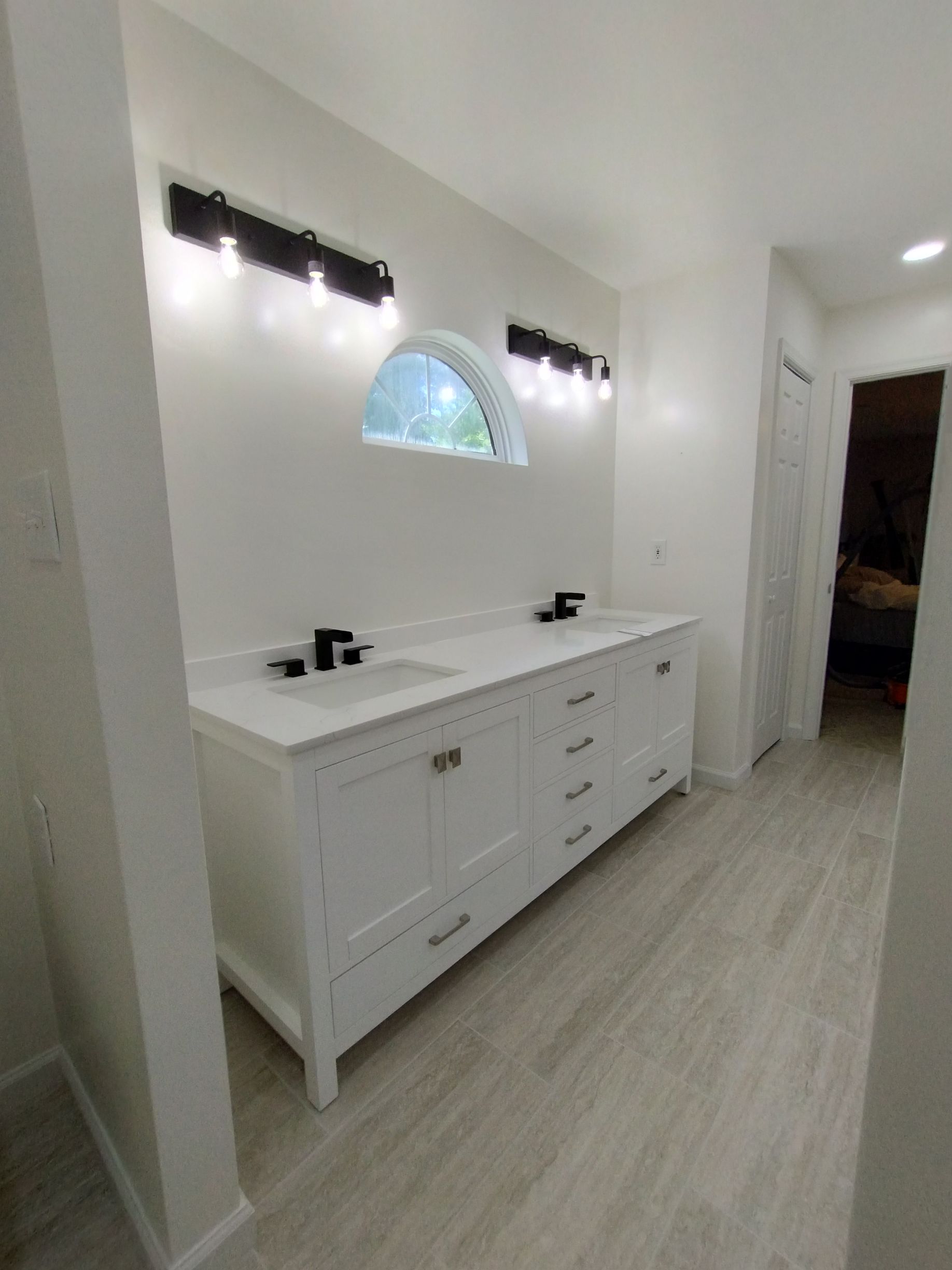 Bright white bathroom with double vanity, wall lights, and a half-circle window