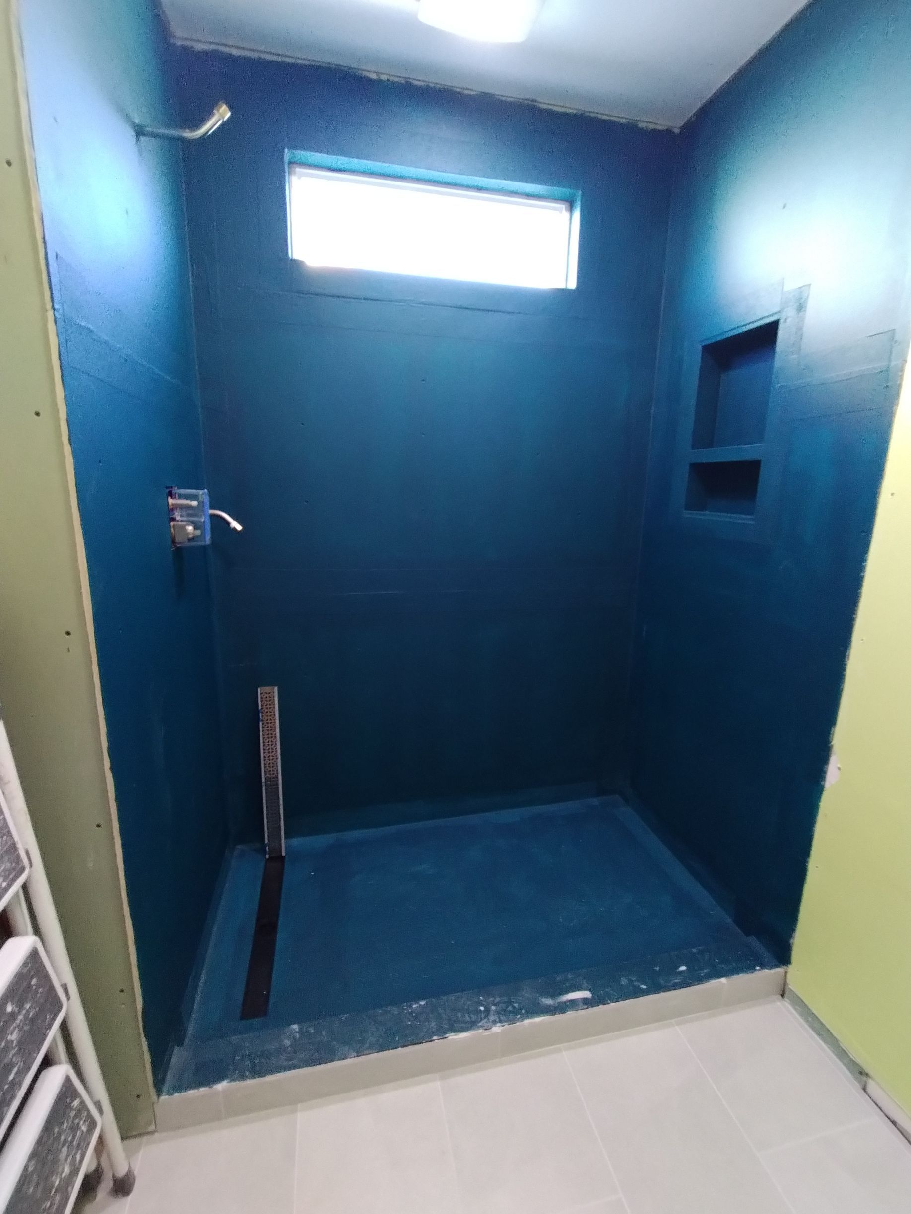 Blue-tiled accessible shower with grab bars, bench, and small high window.