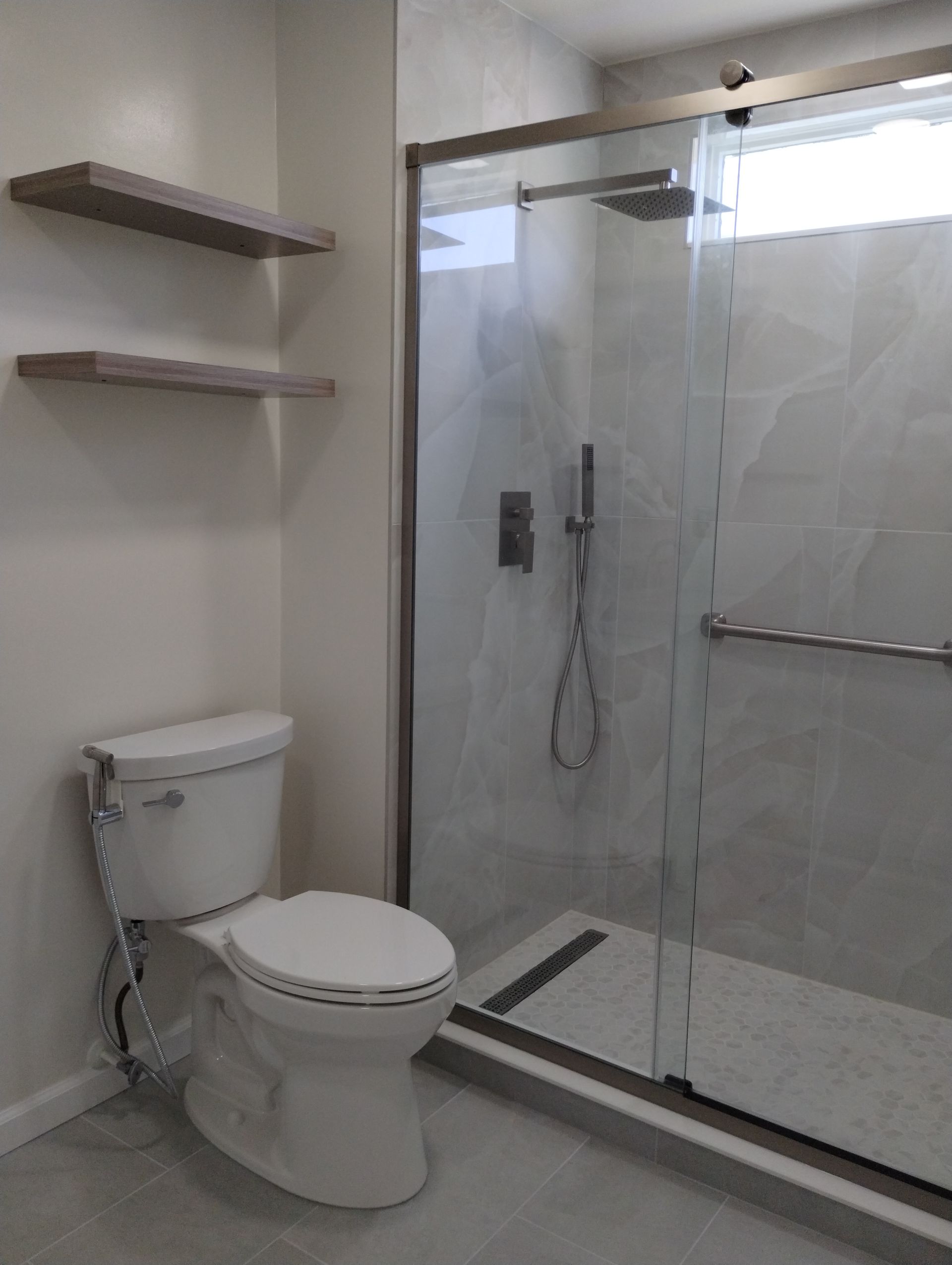 Modern bathroom with a toilet, glass-enclosed shower, and wall shelves on a tiled floor.