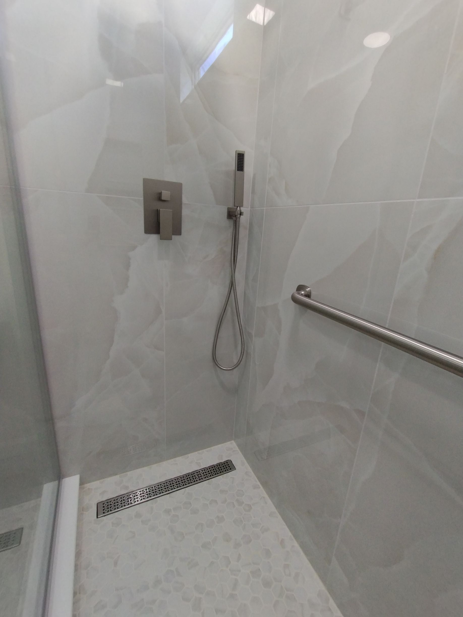 Modern white shower with wall-mounted fixtures, handheld showerhead, and linear drain