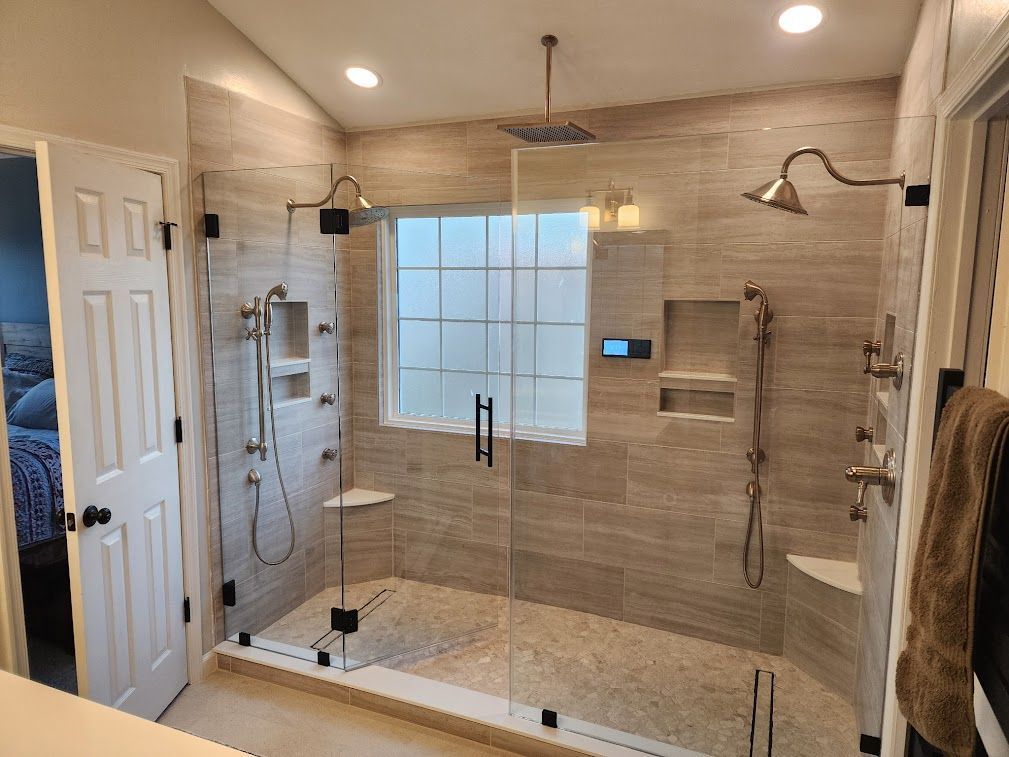 Spacious tiled walk-in shower with glass doors, bench, and chrome fixtures in a bright bathroom