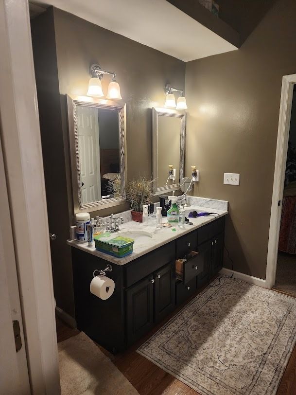 Bathroom vanity with double mirrors, lights, granite countertop, and patterned rug