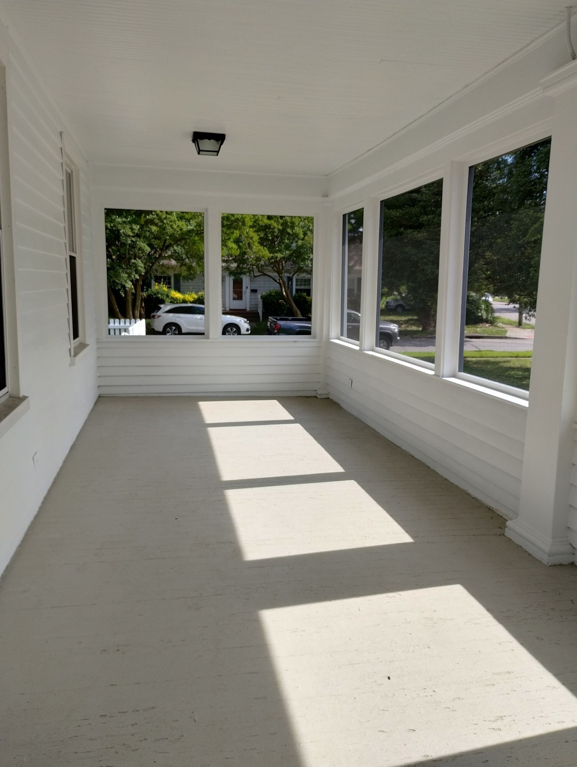 Empty white porch with large windows and sunlight casting long shadows on the floor
