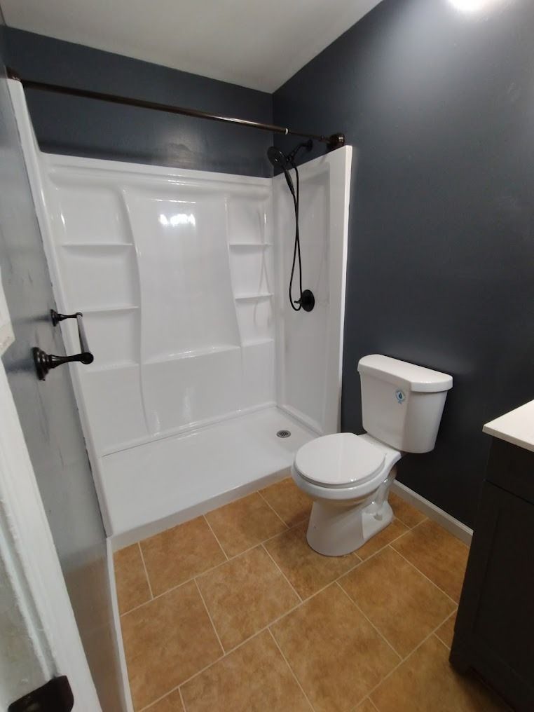 Small bathroom with a walk-in shower, toilet, tan tile floor, and dark gray walls