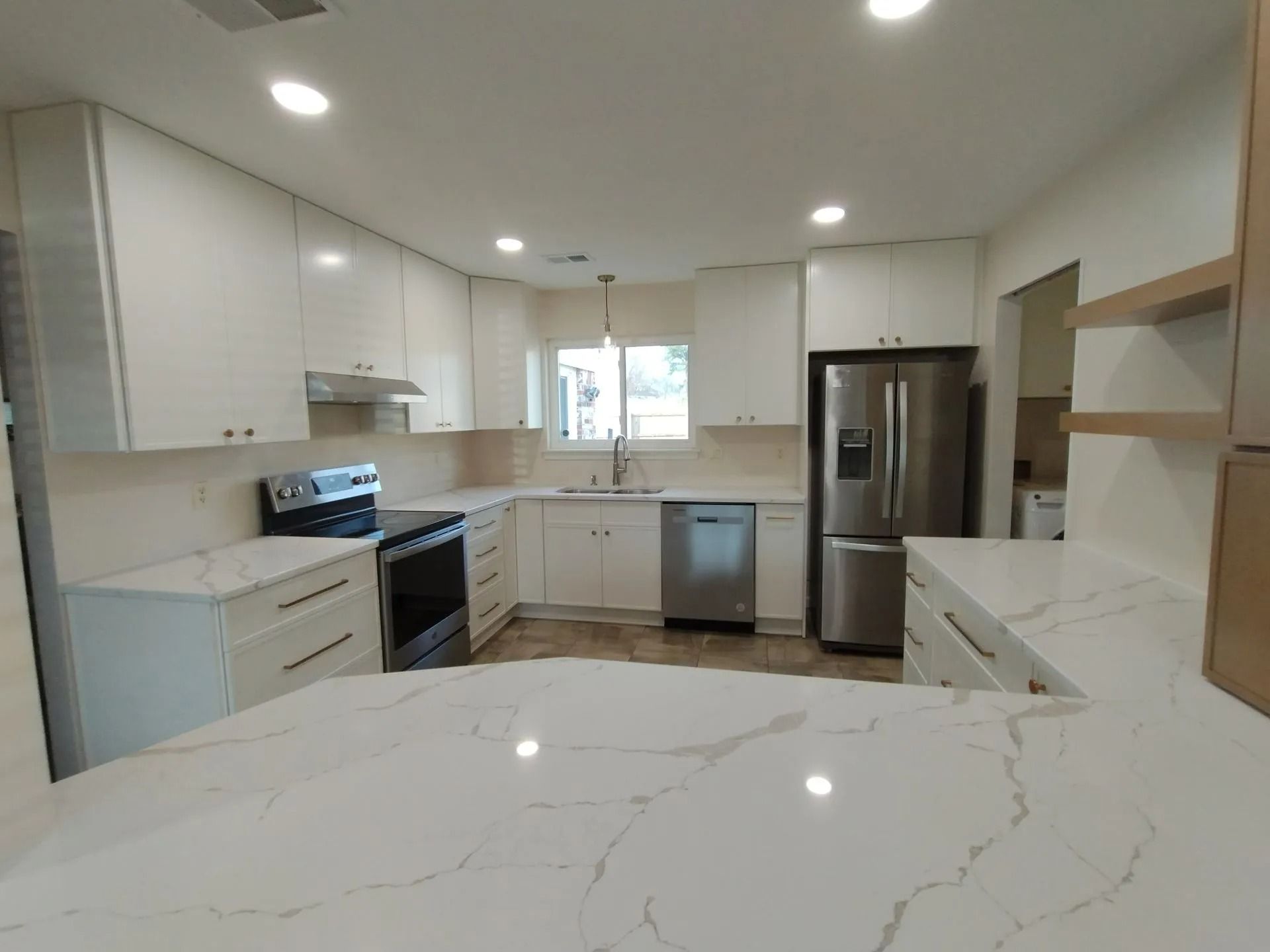 Bright modern kitchen with white cabinets, marble countertop, stainless steel appliances, and recessed lighting