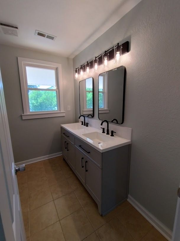 Modern bathroom with double vanity, large mirror, black sconces, and a window letting in daylight