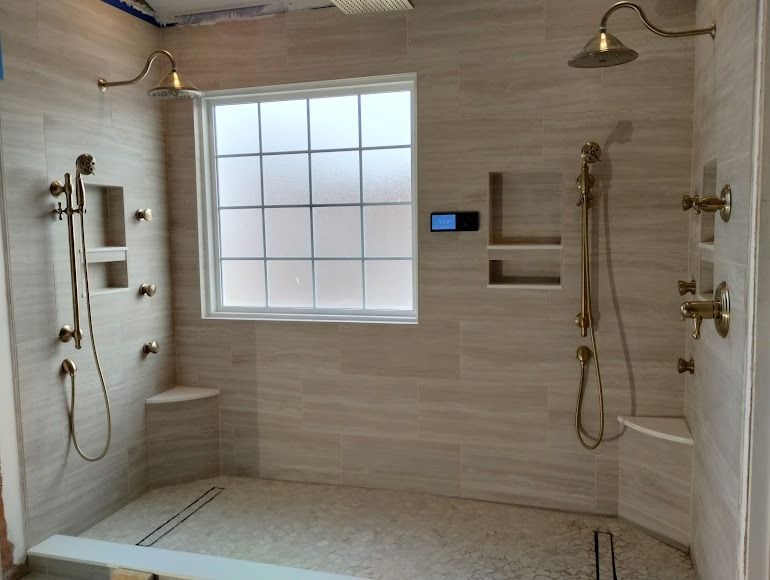 Spacious beige-tiled bathroom with double rain showers, built-in benches, and a frosted window.