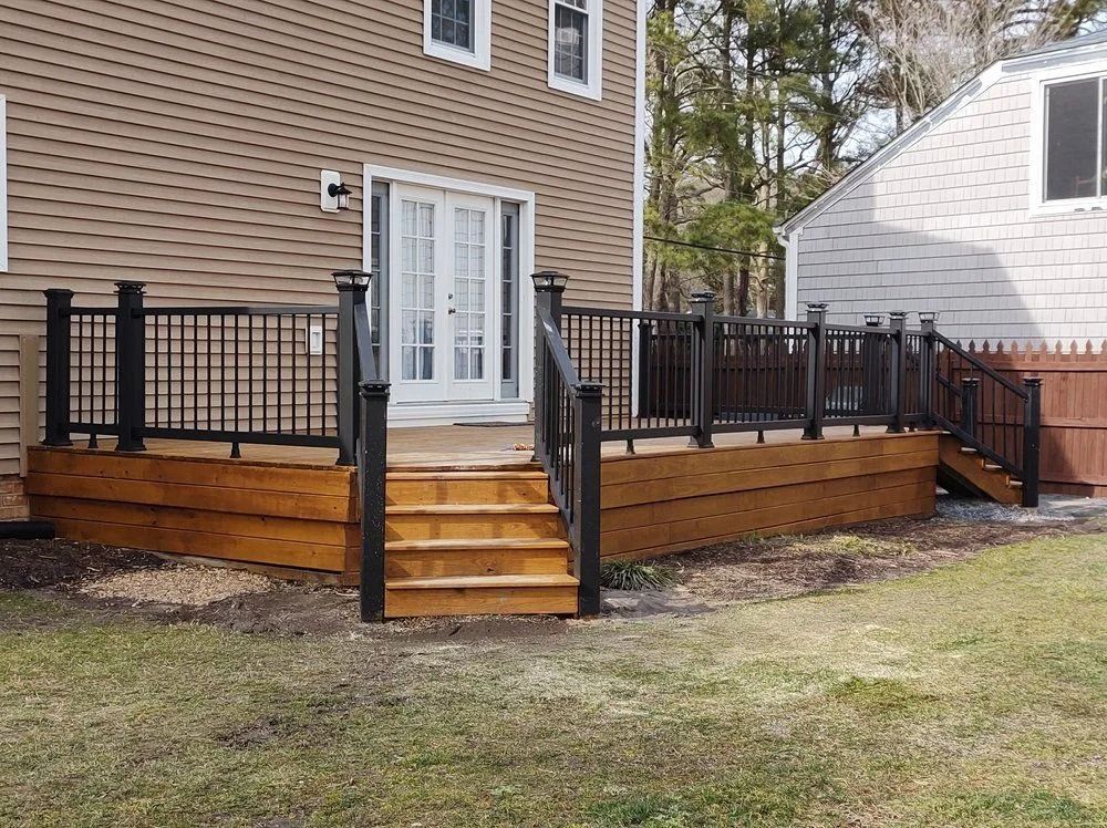 Backyard wooden deck with black railings and stairs leading to a white door on a house