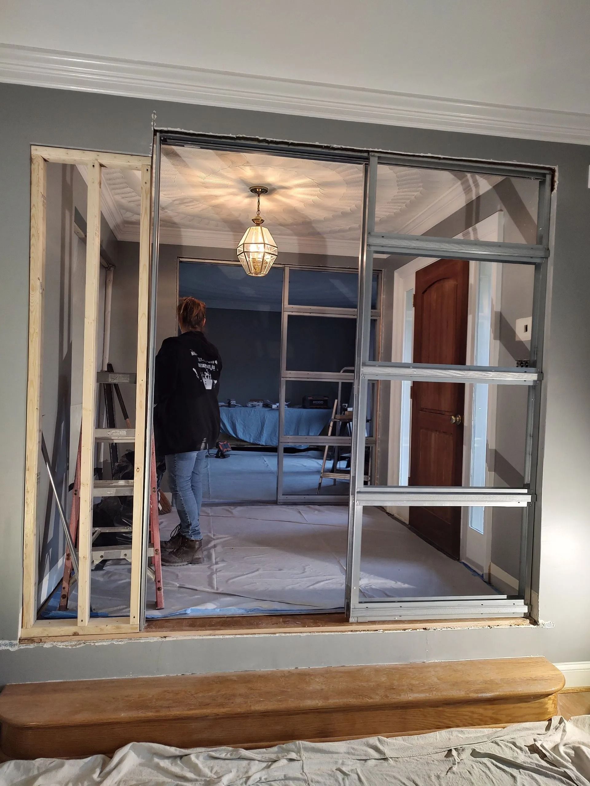 Renovation opening with exposed framing and a worker standing inside a room under a hanging light.
