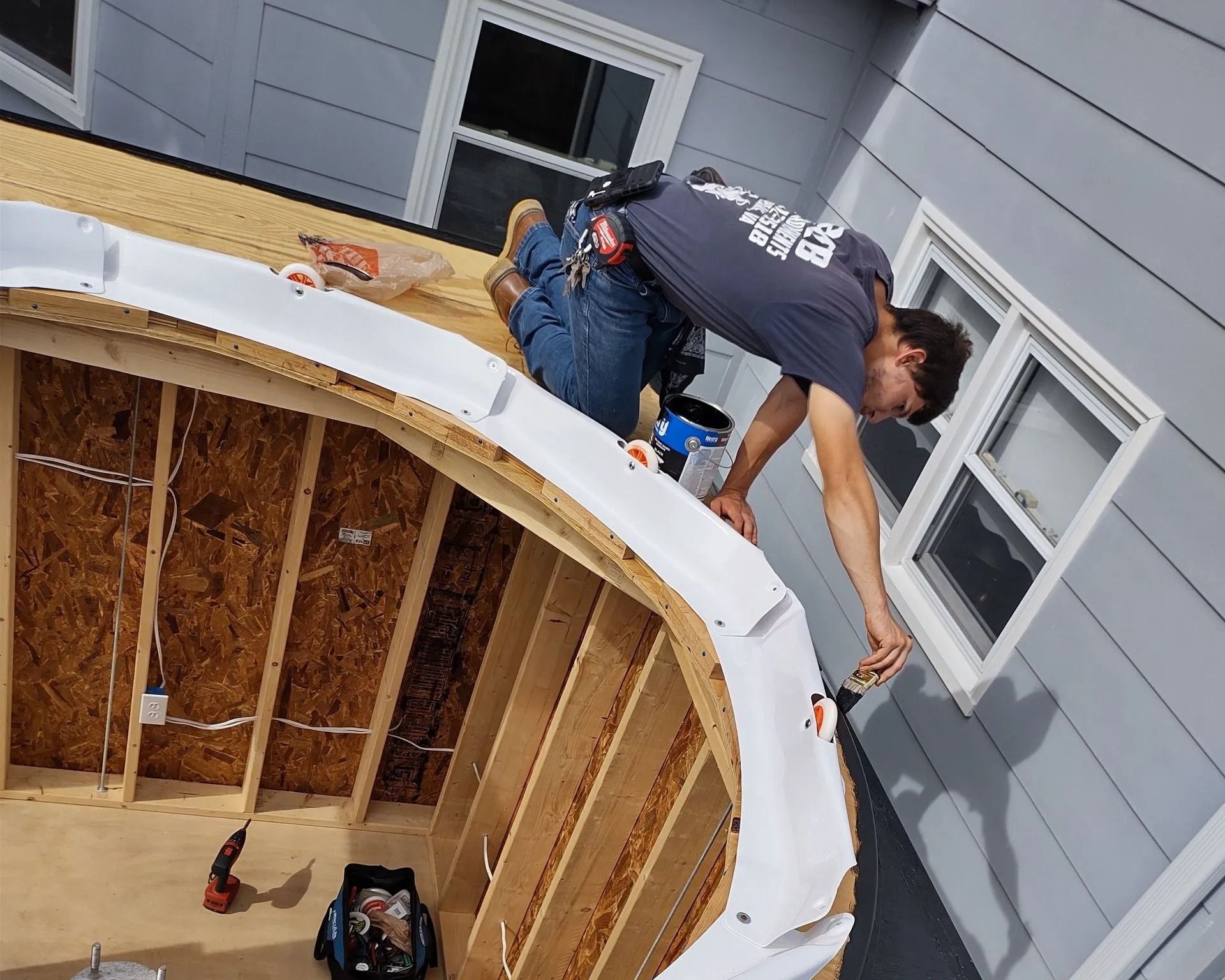 Worker installing roofing on a curved wooden structure beside gray house siding
