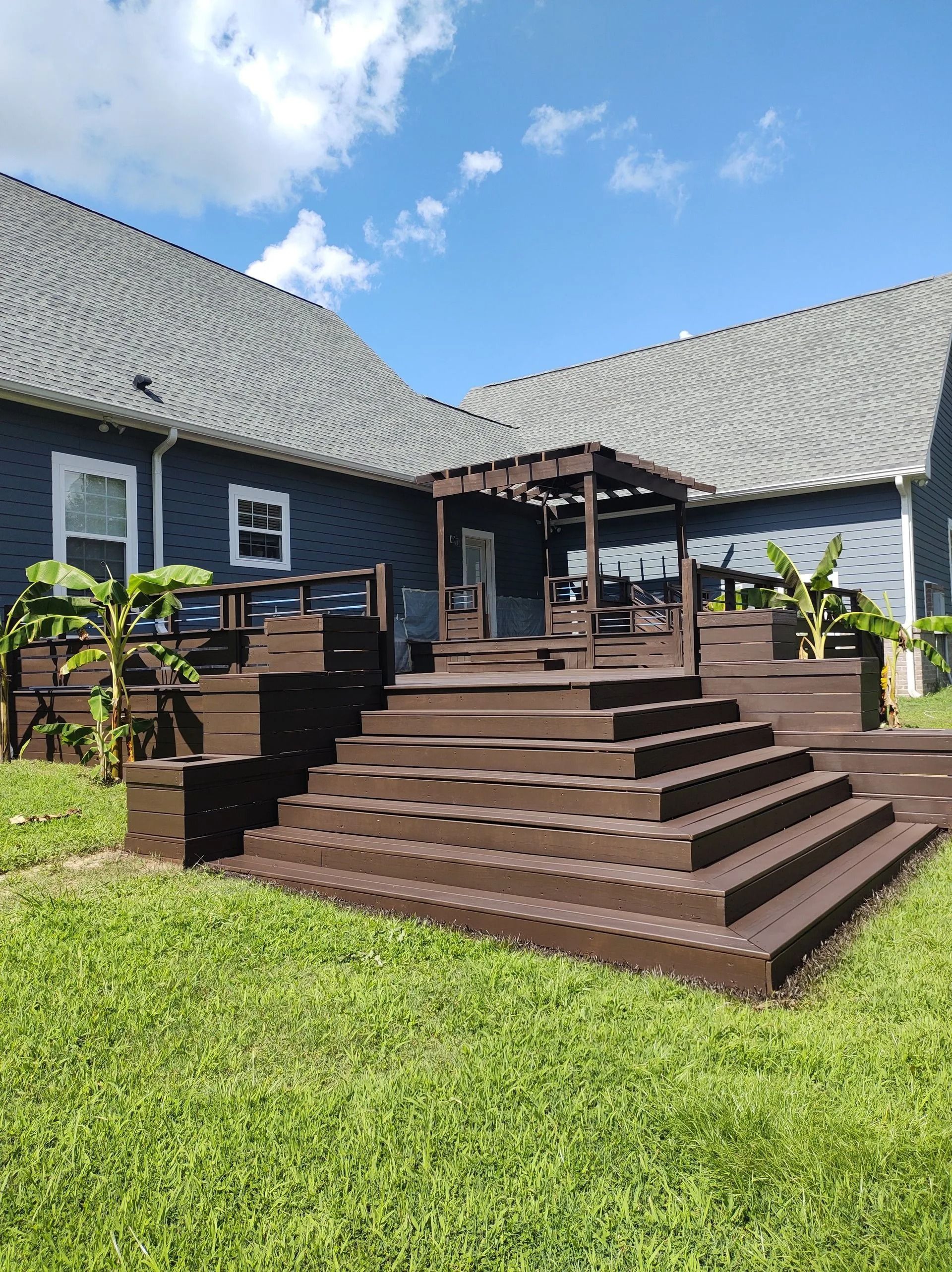 Dark house exterior with wide wooden steps, porch, and green lawn under a blue sky