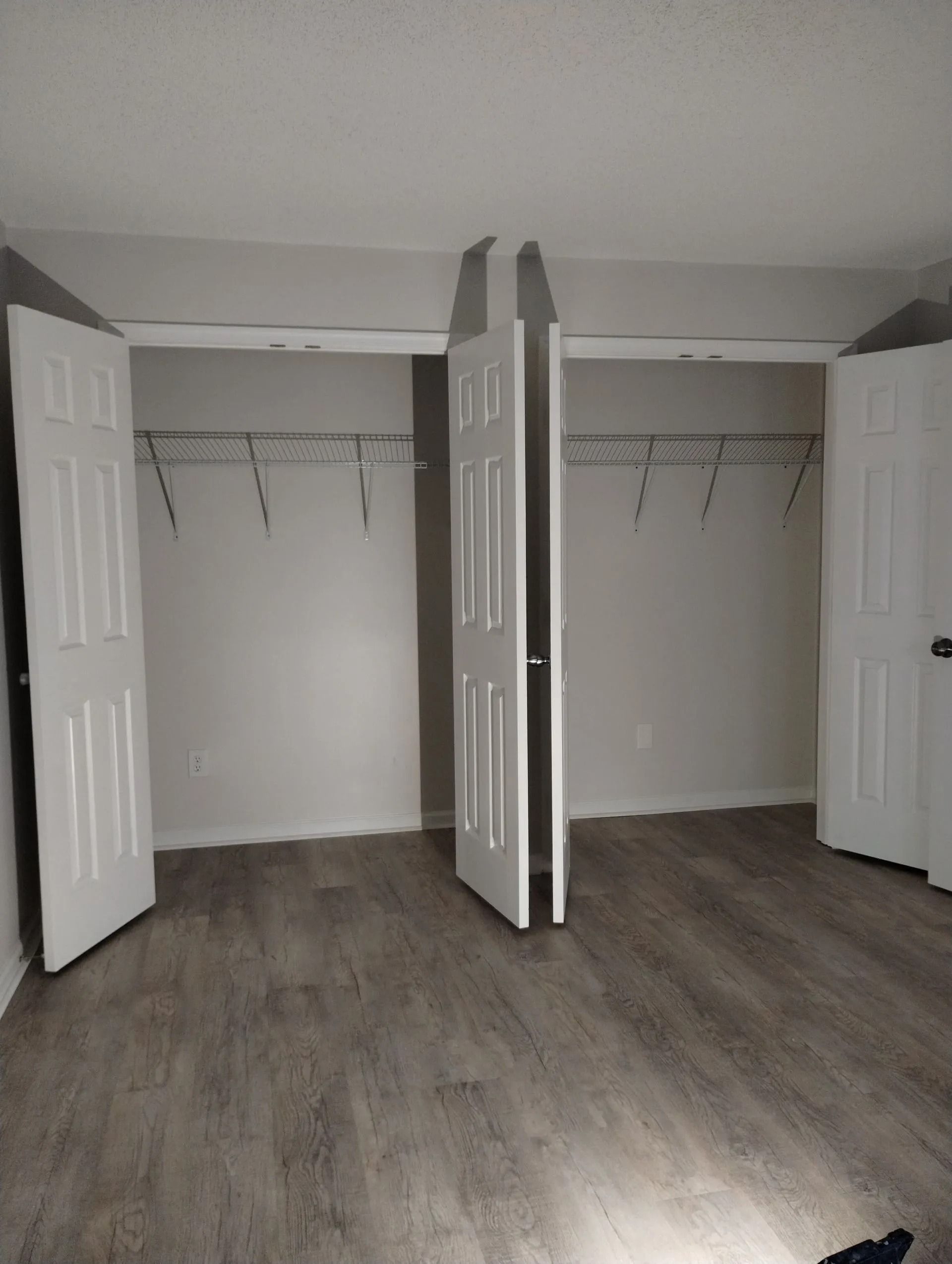Empty bedroom with open closet doors and gray wood-look flooring