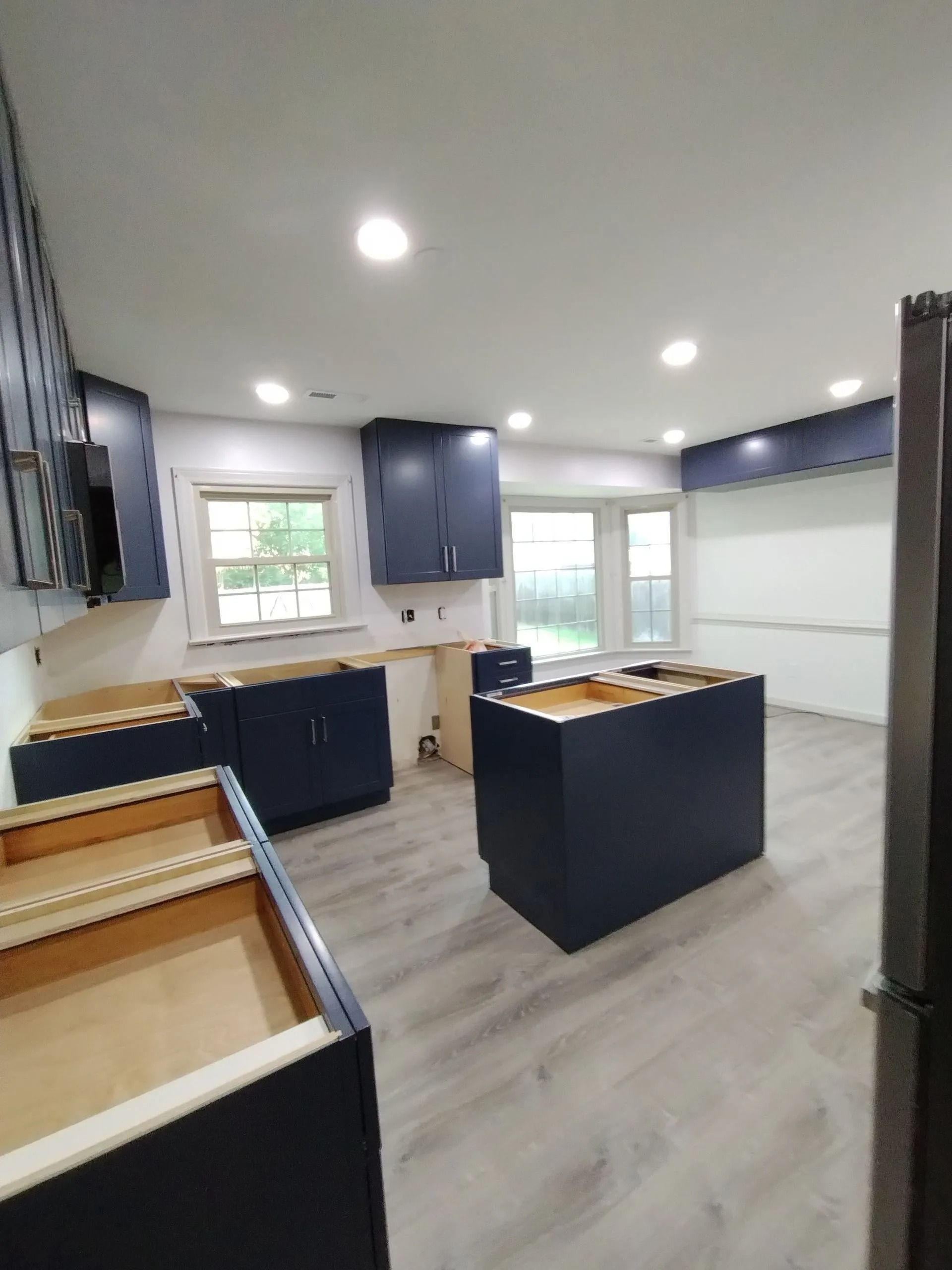Modern kitchen under renovation with dark cabinets, light wood floors, white walls, and an island countertop
