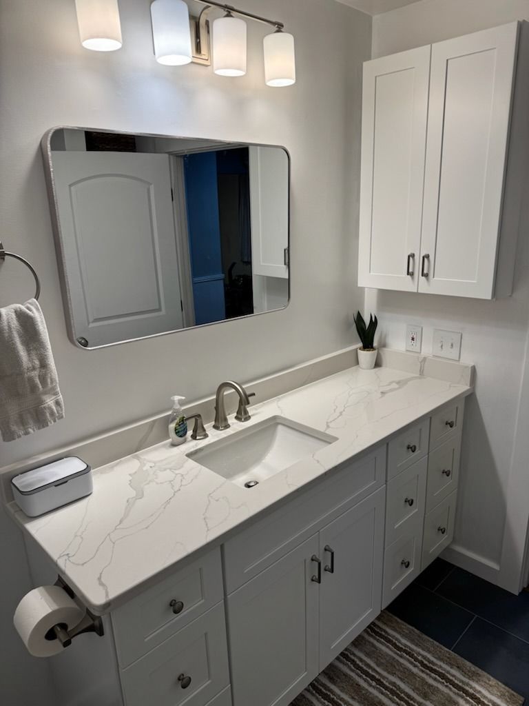 Modern gray bathroom vanity with white countertop, mirror, lights, and wall cabinet