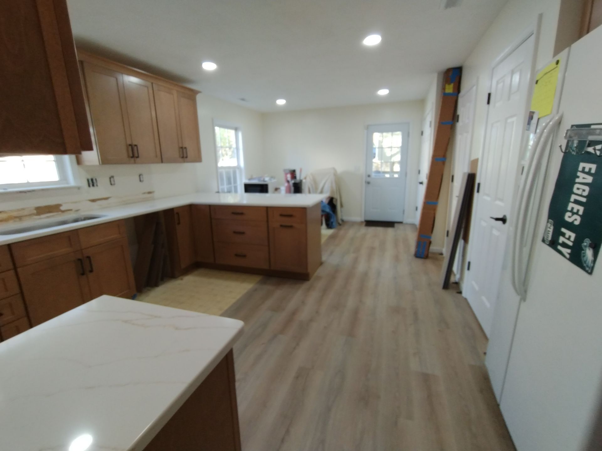Bright kitchen with wood cabinets, white countertops, recessed lights, and a white refrigerator.
