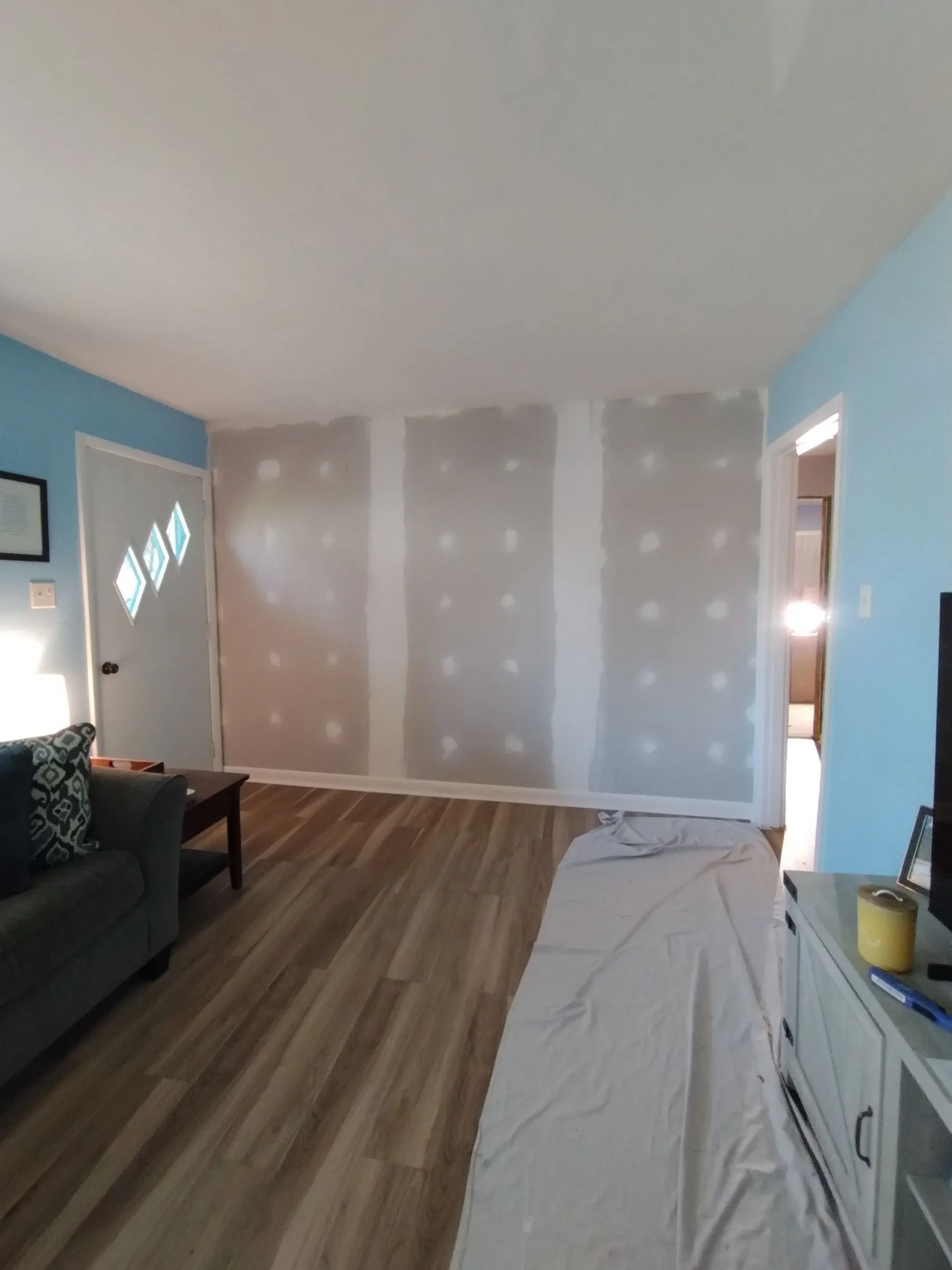 Living room with blue walls, wood floor, and unfinished beige drywall in the back.