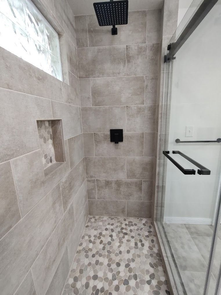 Modern bathroom shower with gray tile, mosaic floor, glass door, and rain showerhead.