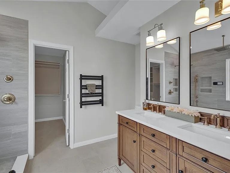 Bright bathroom with wood vanity, double mirrors, white walls, and walk-in shower.