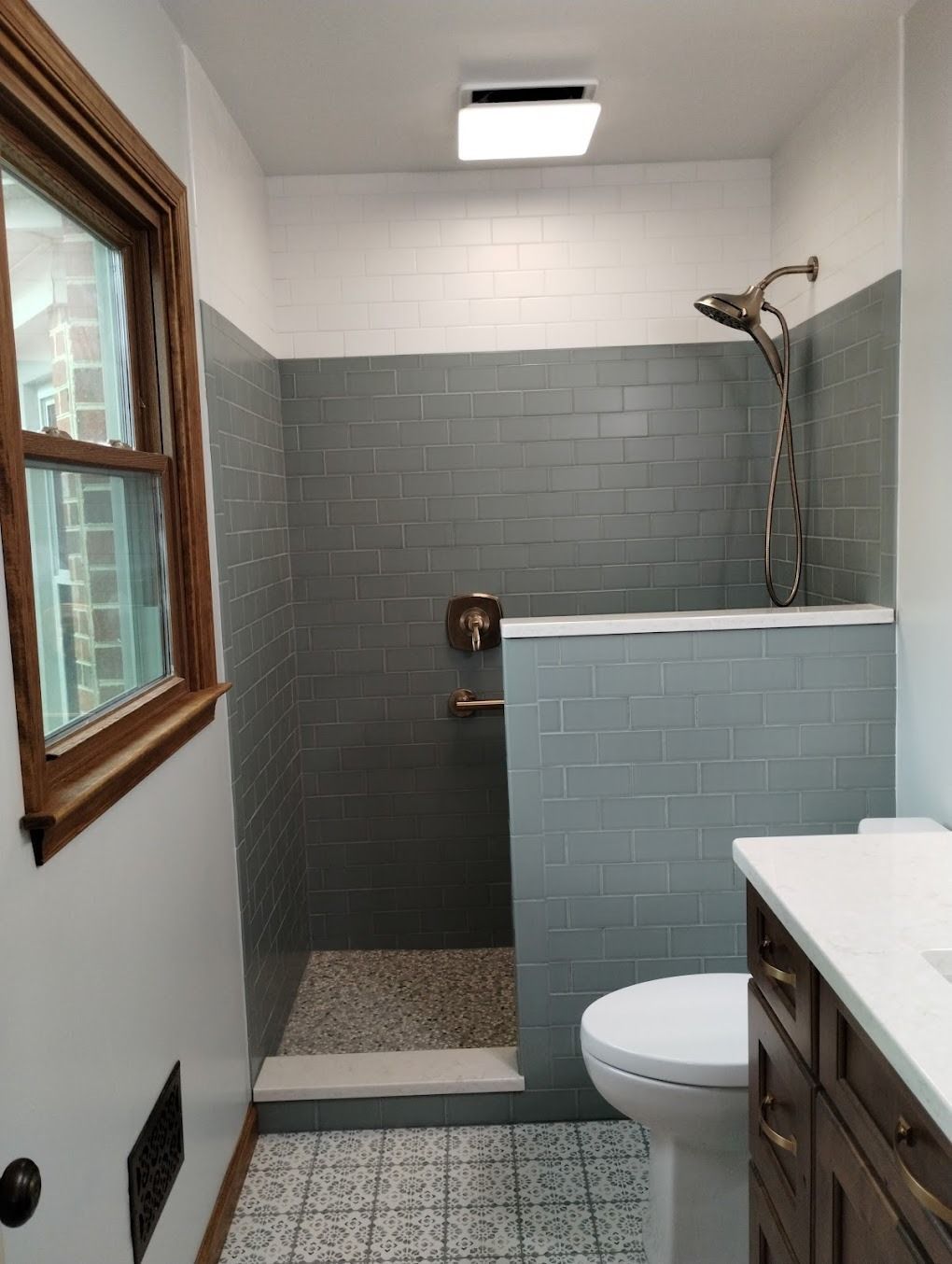 Small bathroom with a gray-tiled walk-in shower, toilet, vanity, and window.