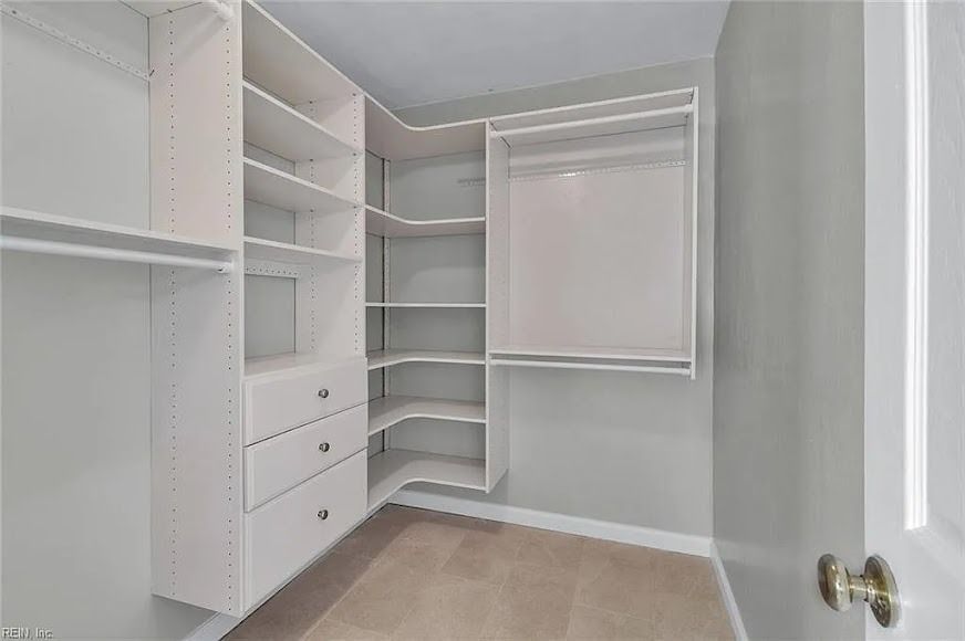Empty walk-in closet with white shelves, drawers, and hanging rods on light gray walls.