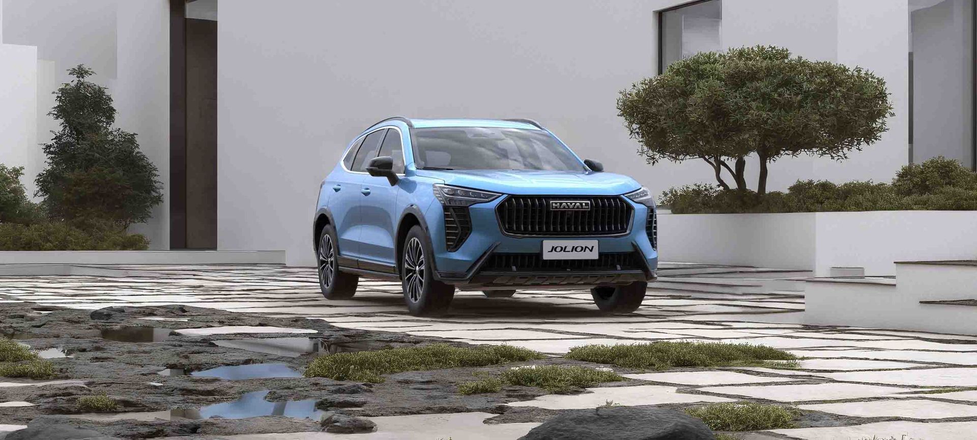 Un SUV azul circula por un camino de piedra mojada junto a edificios blancos y árboles.