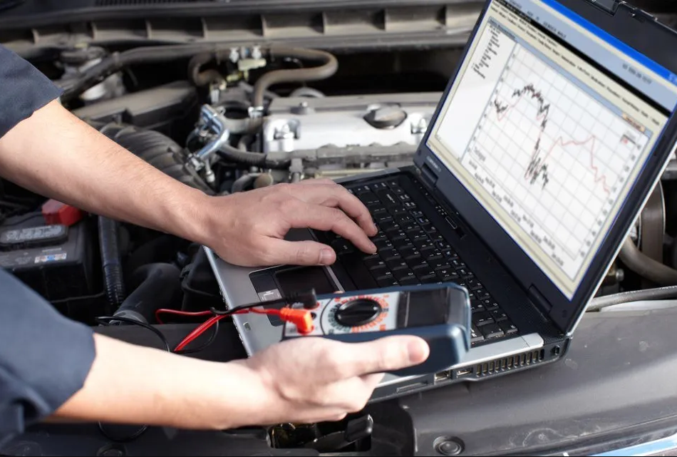 Meccanico che utilizza un computer portatile e un dispositivo diagnostico per controllare il motore di un'auto.