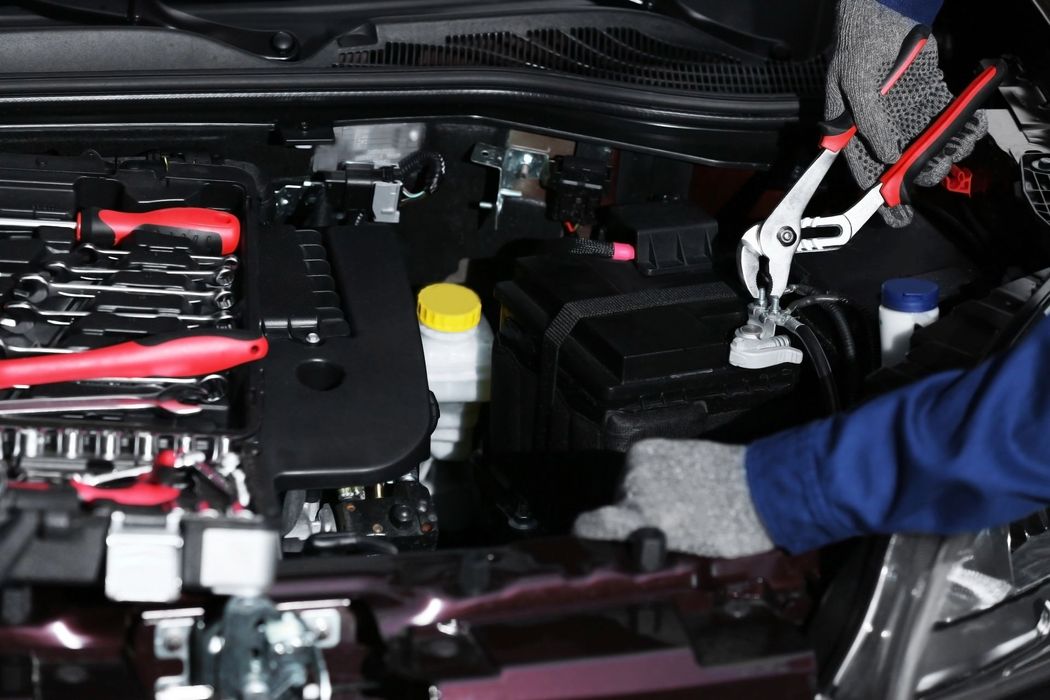 Meccanico al lavoro nel vano motore di un'auto con attrezzi e cavi di avviamento collegati