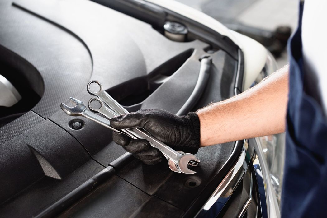 Meccanico con i guanti che usa le pinze per lavorare sul motore di un'auto in un'officina.