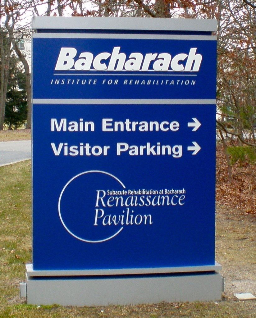 Blue sign for Bacharach Institute for Rehabilitation, pointing towards main entrance and visitor parking.