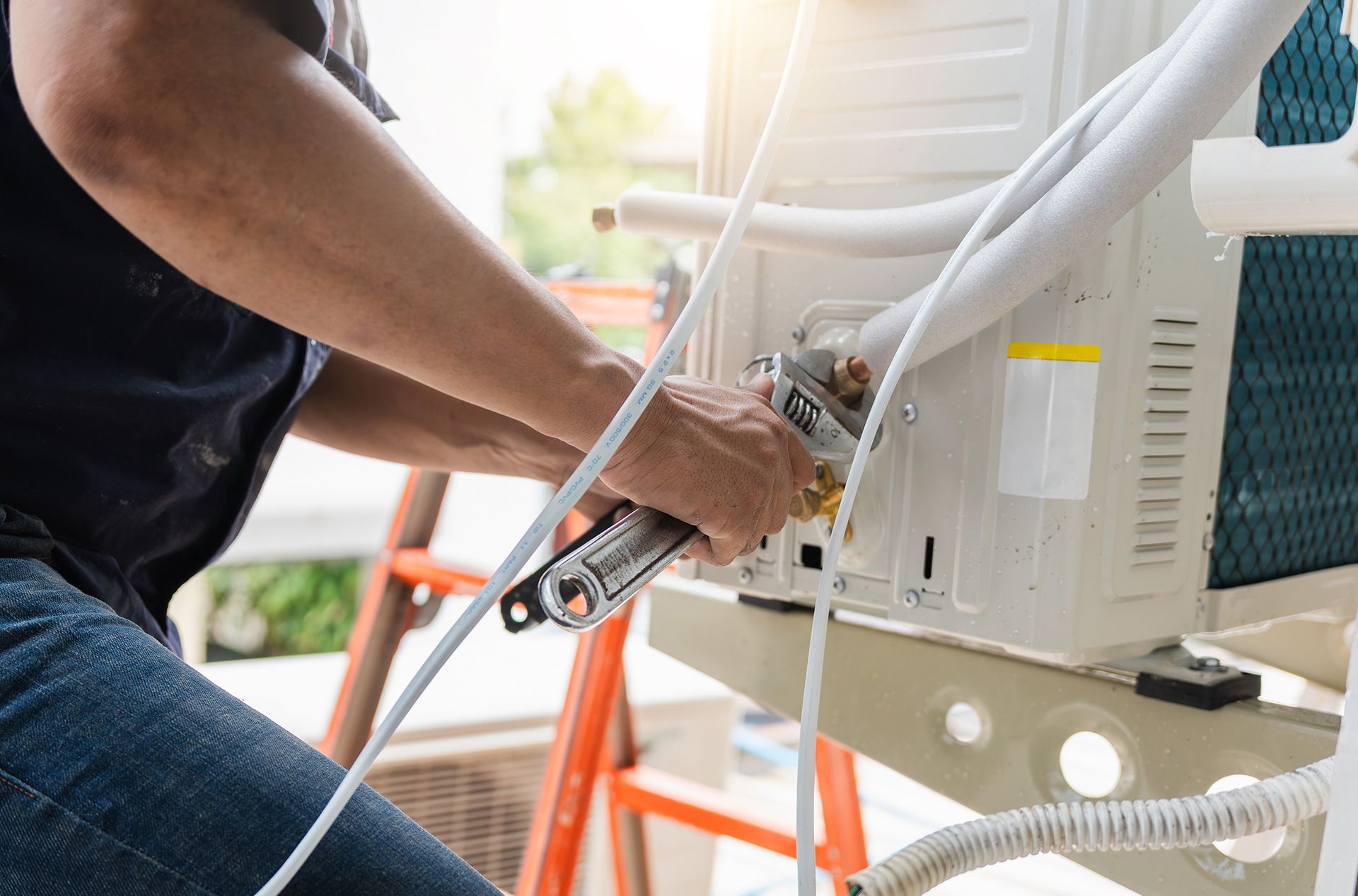 Technician tightening an outdoor air conditioner unit with a wrench and hose attached