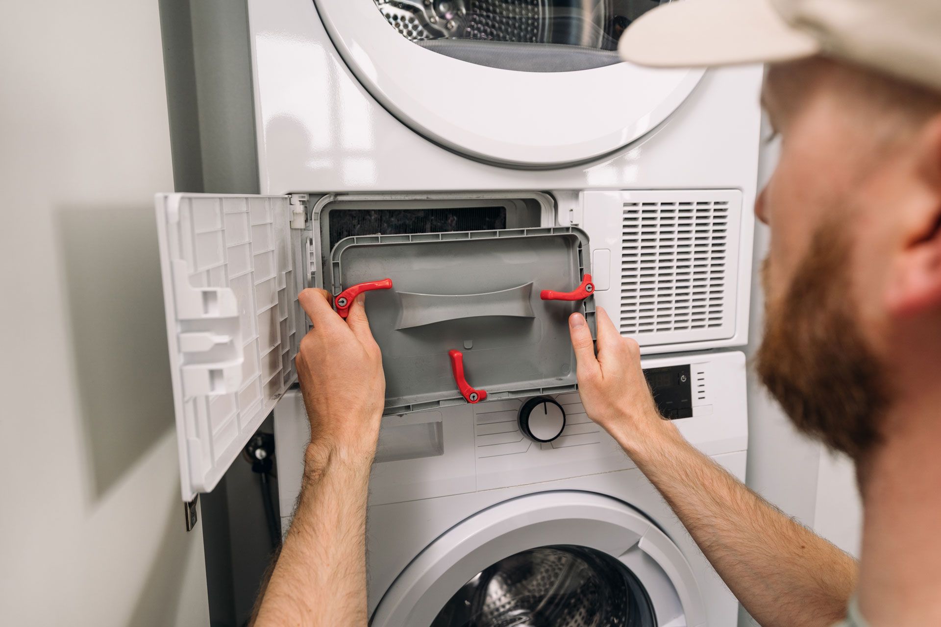 Person installing a dryer vent hose behind a stacked washer and dryer
