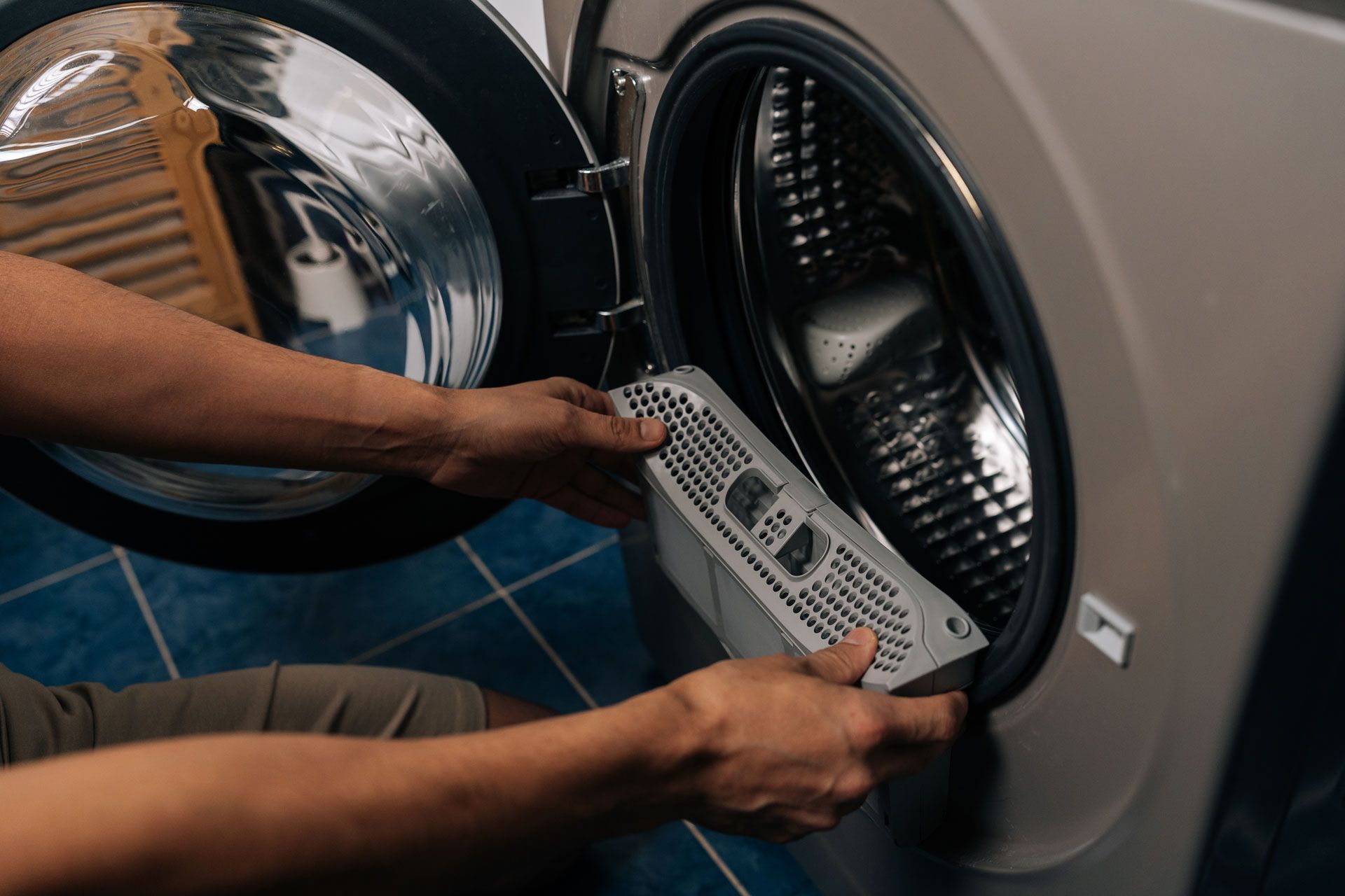 Person holding a washing machine control panel while repairing an open front-loading washer