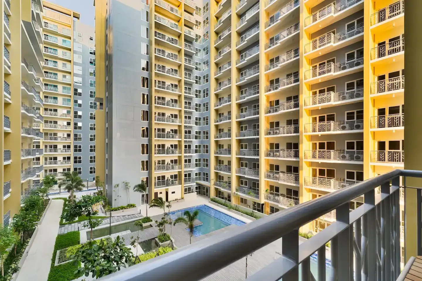 A balcony overlooking a large apartment building with a 
 swimming pool.  The Den at Bayshore Luxe by Prime, Manila