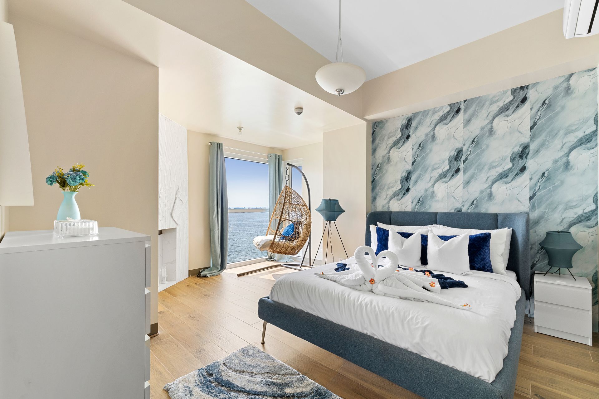 Bedroom decorated in blues and white with a suspended bucket chair at the window for ocean views 