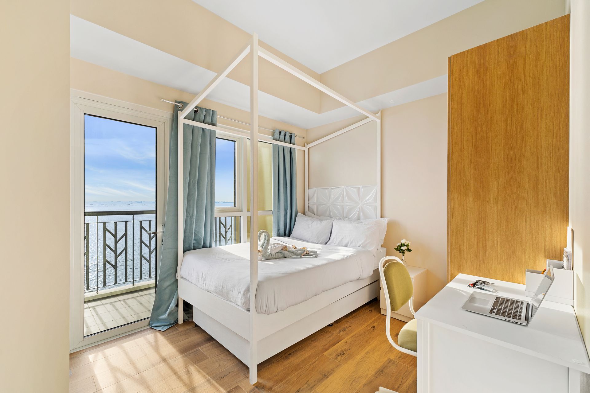 Bedroom with four poster bed, with white linens, a wardrobe, desk and balcony door 