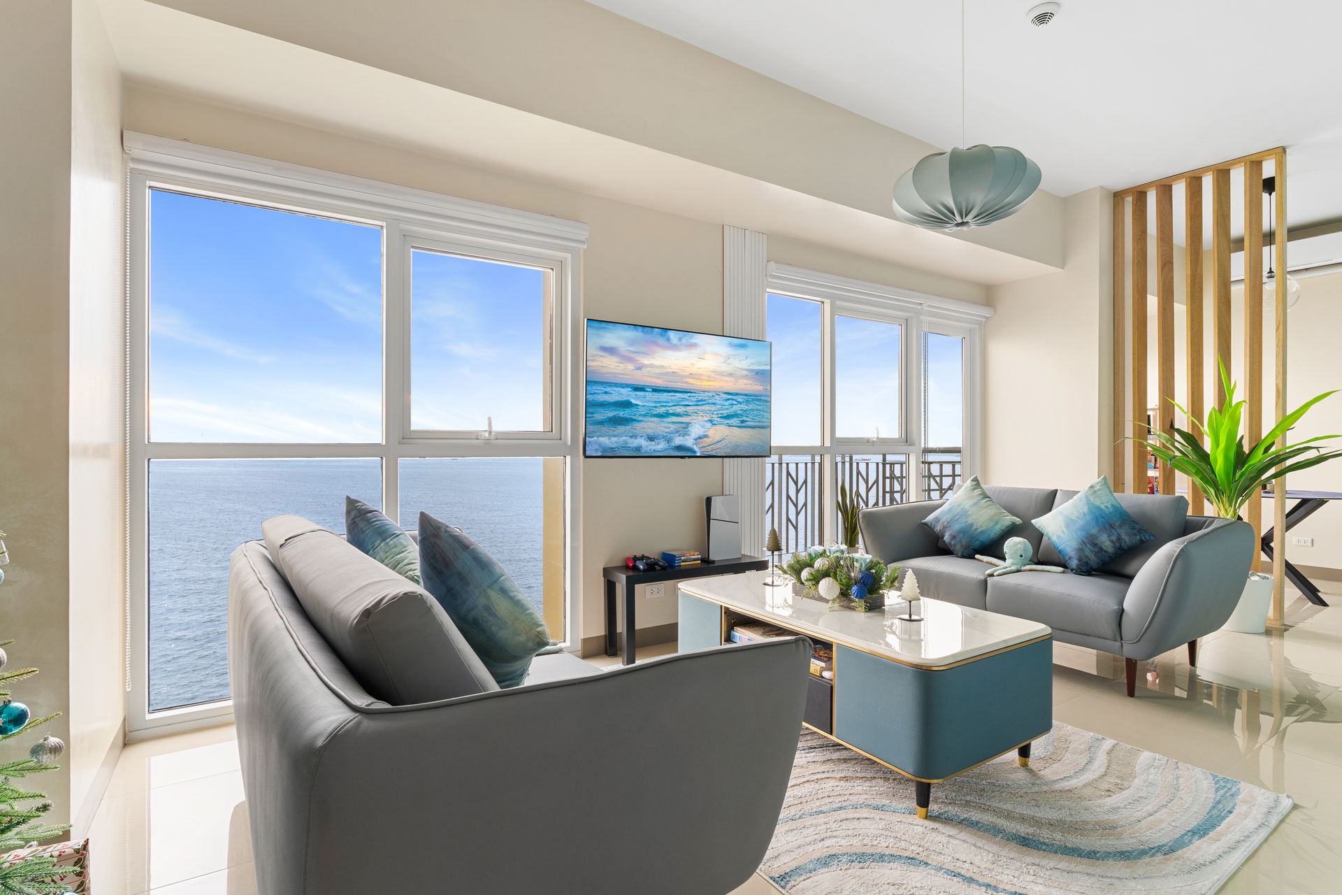 Living room with ocean views, gray sofa's a blue and white coffee table, a rug & TV