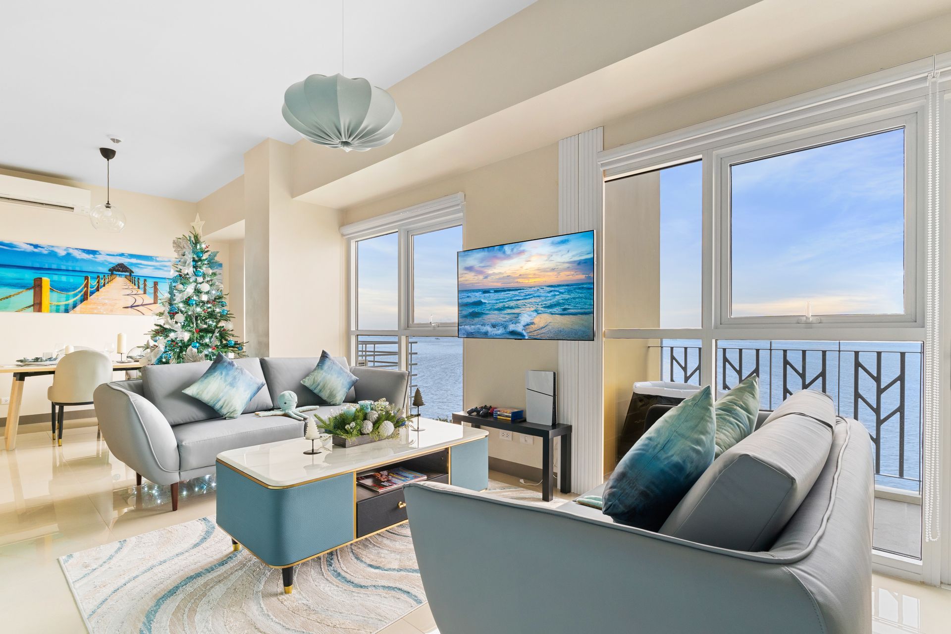 Living room with ocean views, gray sofa's a blue and white coffee table, a rug & TV