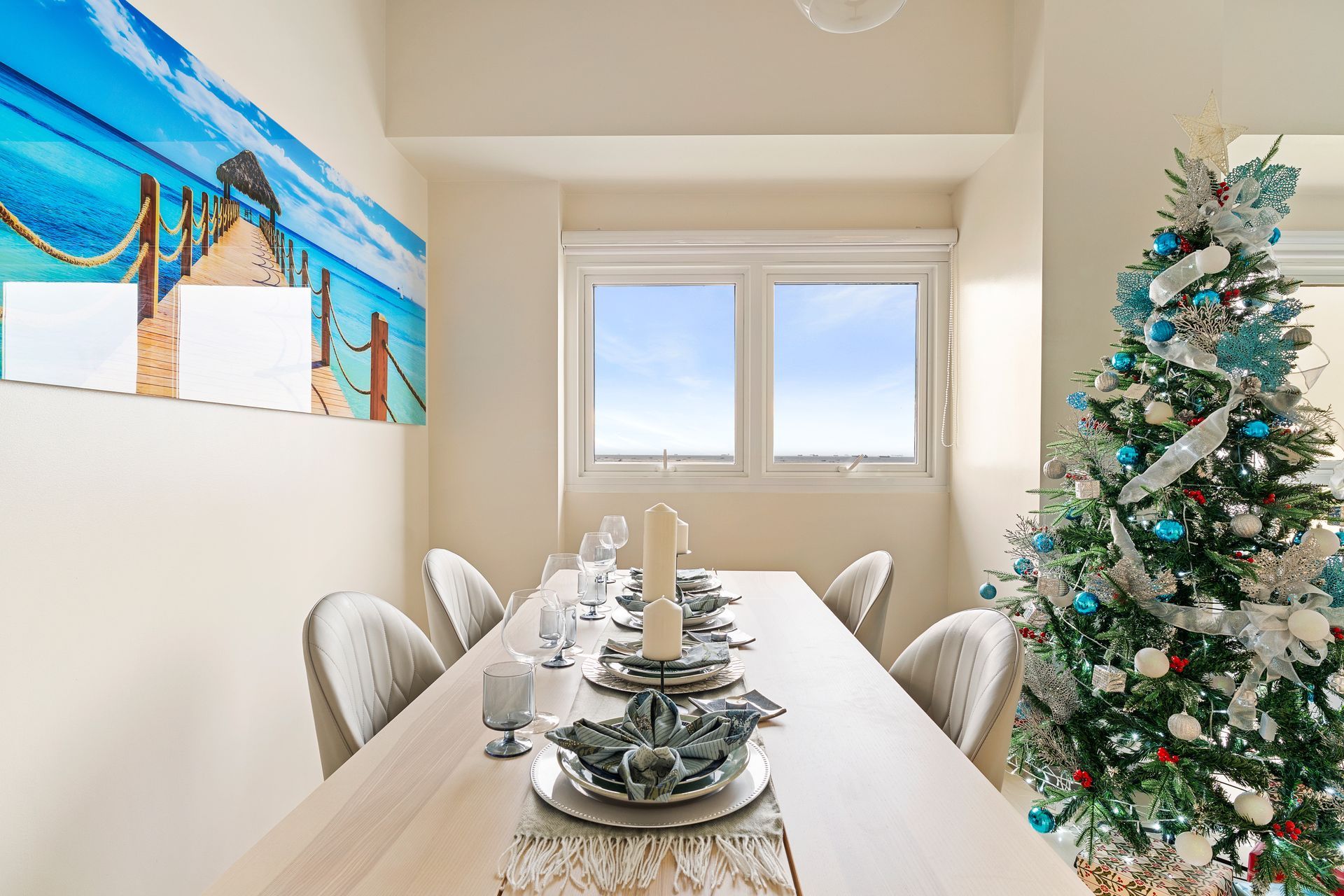 Long white dining table, with gray faux leather chairs, a photo of a tropical dock on the wall on the left