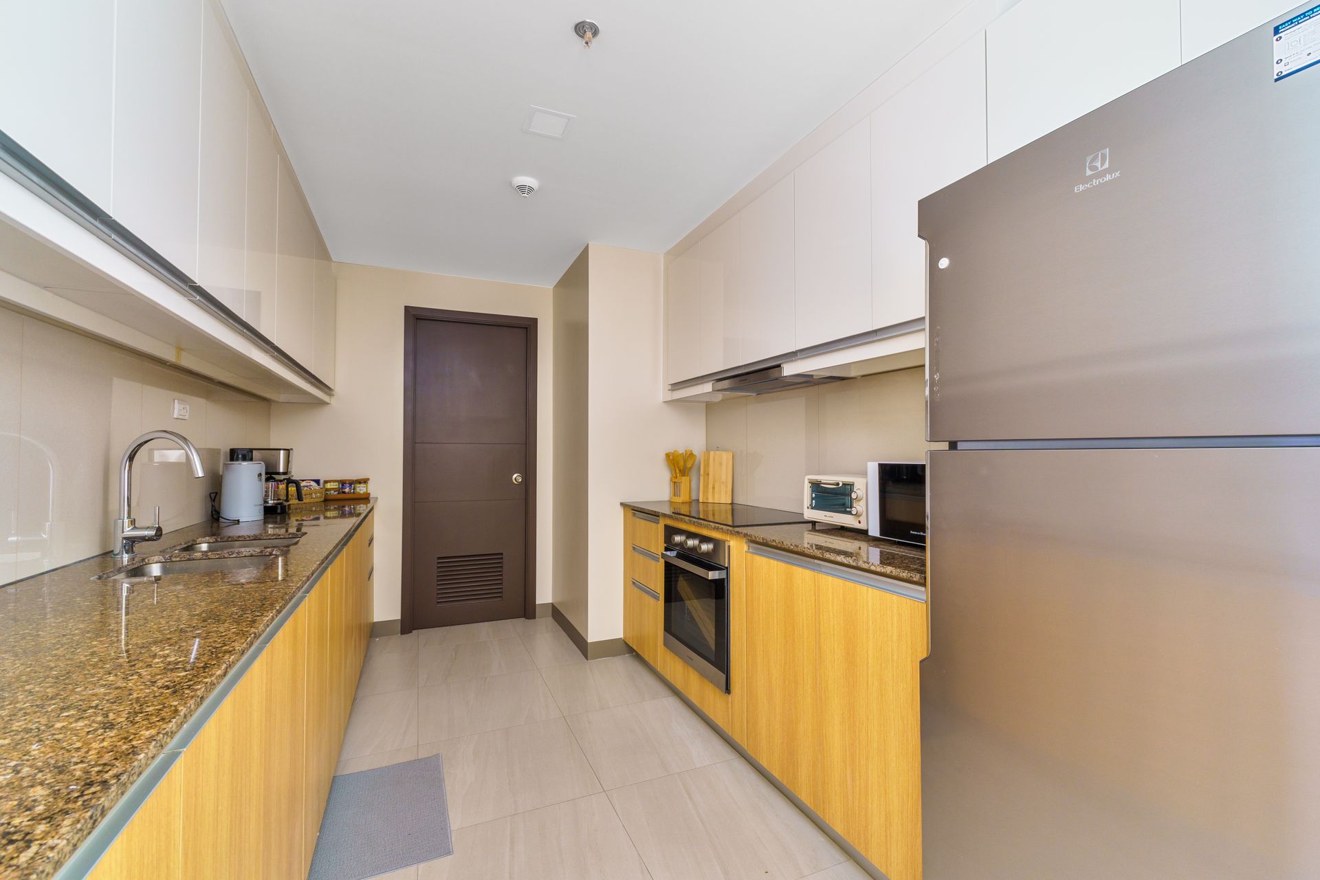 Long galley style kitchen with counter top, sink to the left, oven,  hobs and fridge to the right