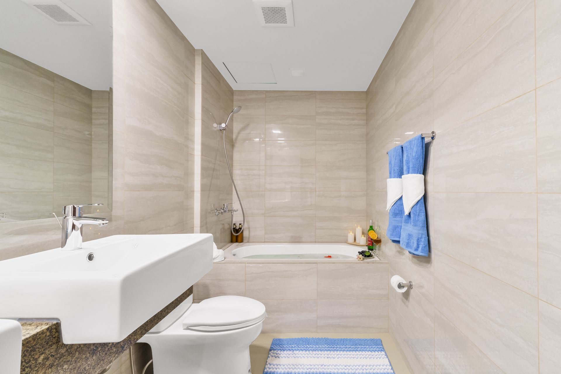 Long bathroom with white sink, toilet and a bath tub with shower over