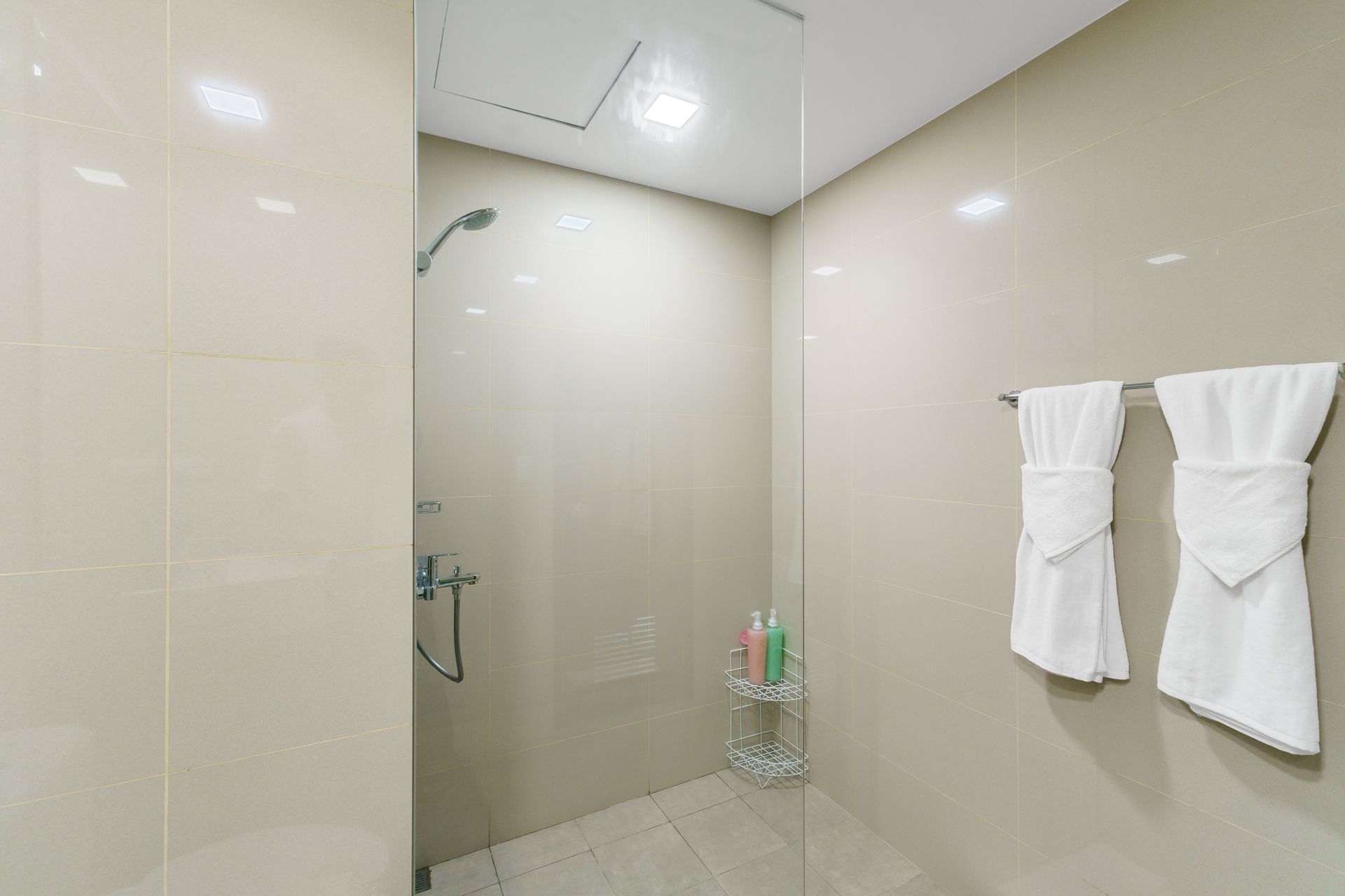 Beige walkin shower with glass door and white towels hanging from a towel rail