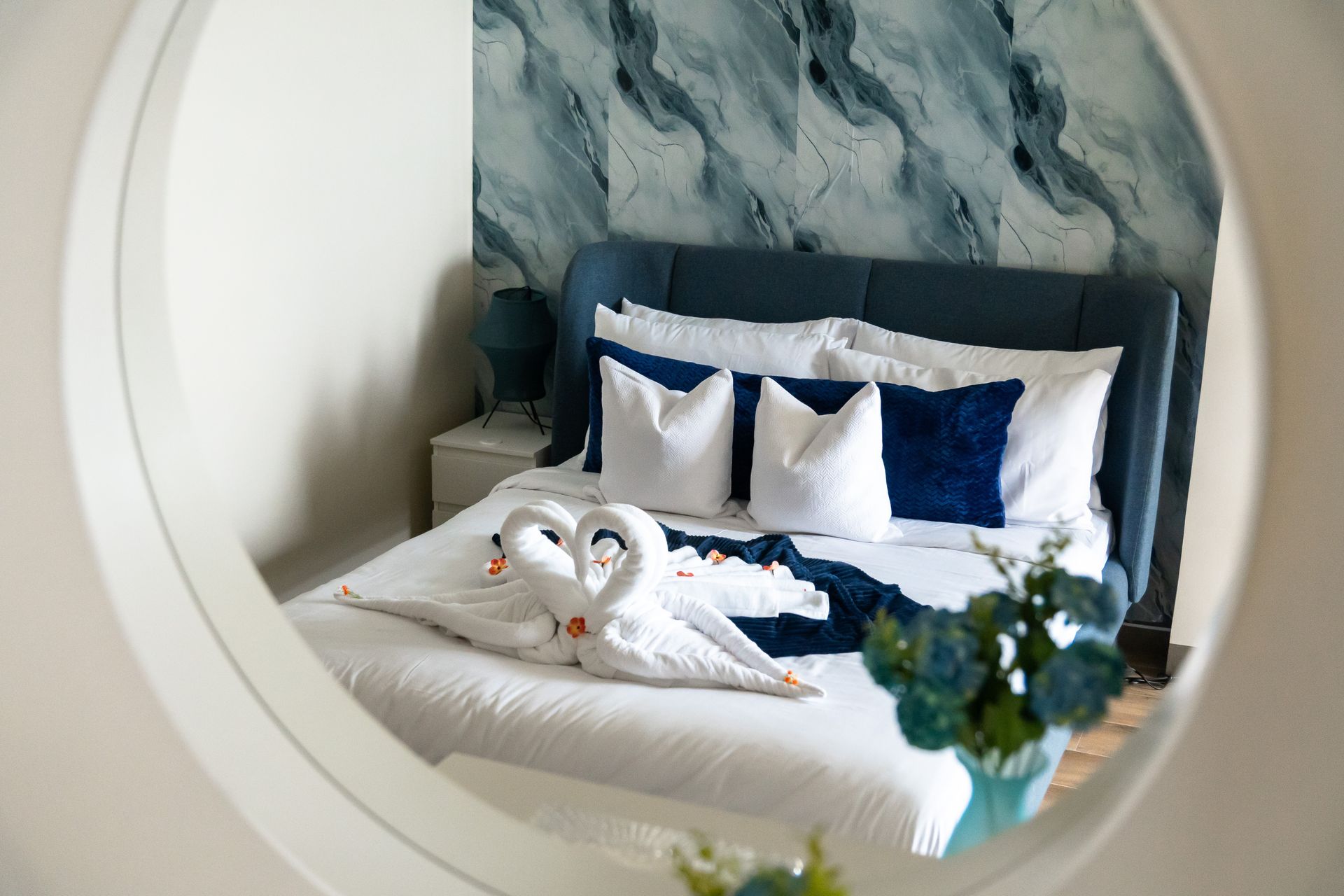 Bed decorated in blues and white linens & cushions taken from a mirror view