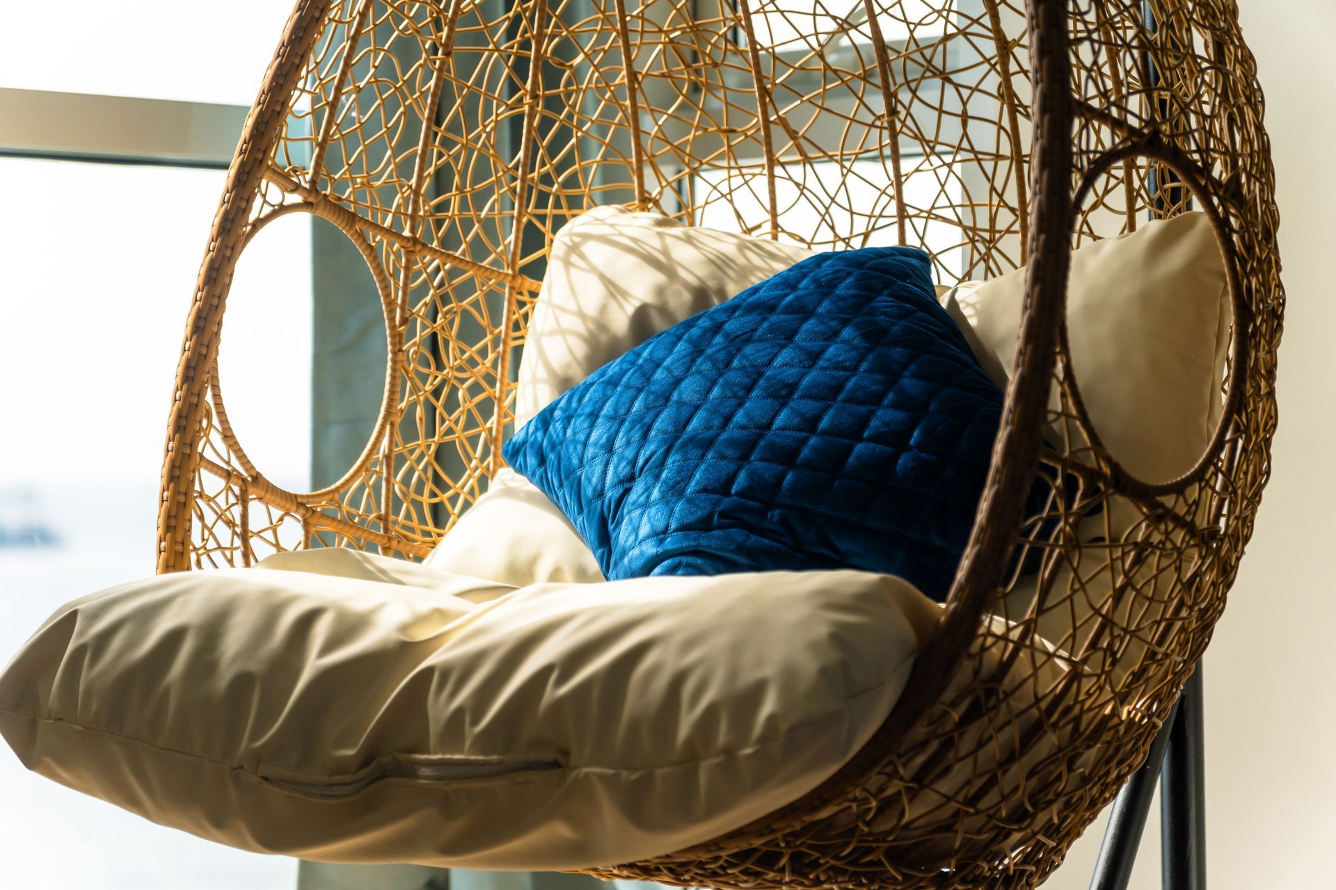A suspended bucket chair with a blue cushion, at a window with ocean views 