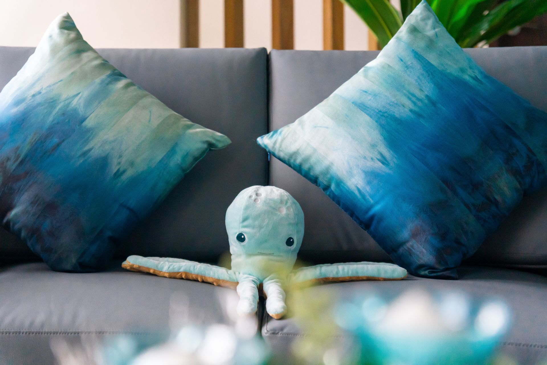 A plushie light blue octupus on  a gray sofa with two blue ombre effect cushions